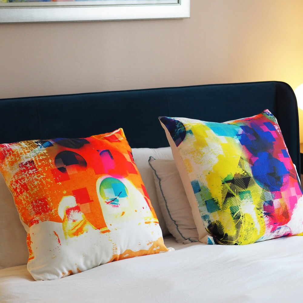 A pair of bright large cushions side by side on a white bed with blue headboard