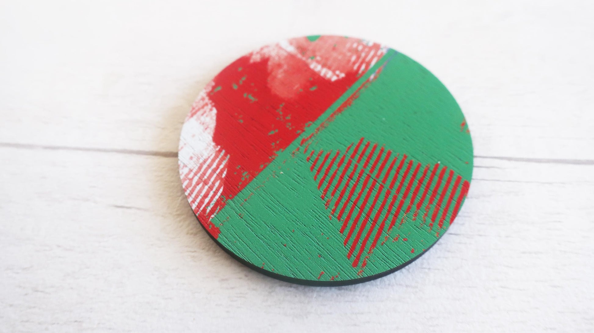 Round brooch with red and green design on a white wooden surface