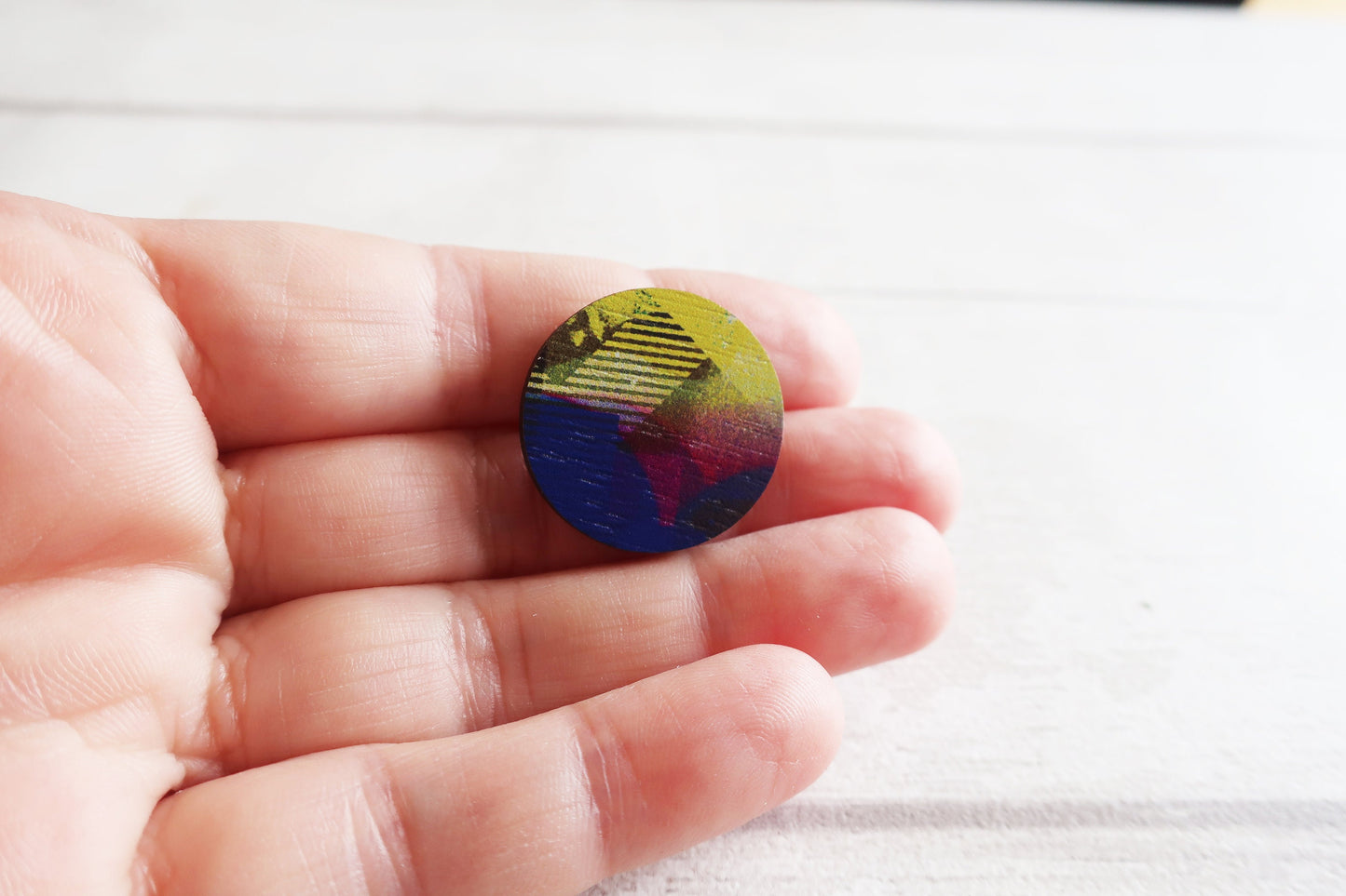 Colorful circular pin badge held in a hand against a white background