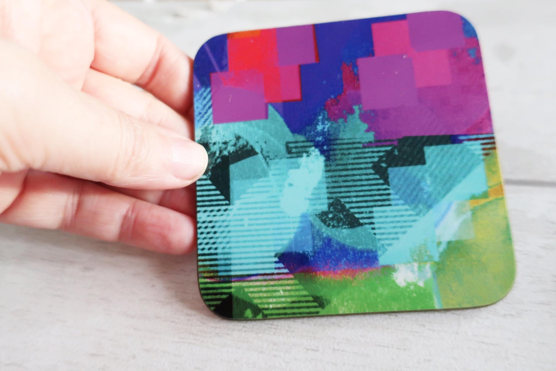 Colorful abstract coaster held by a hand on a light background