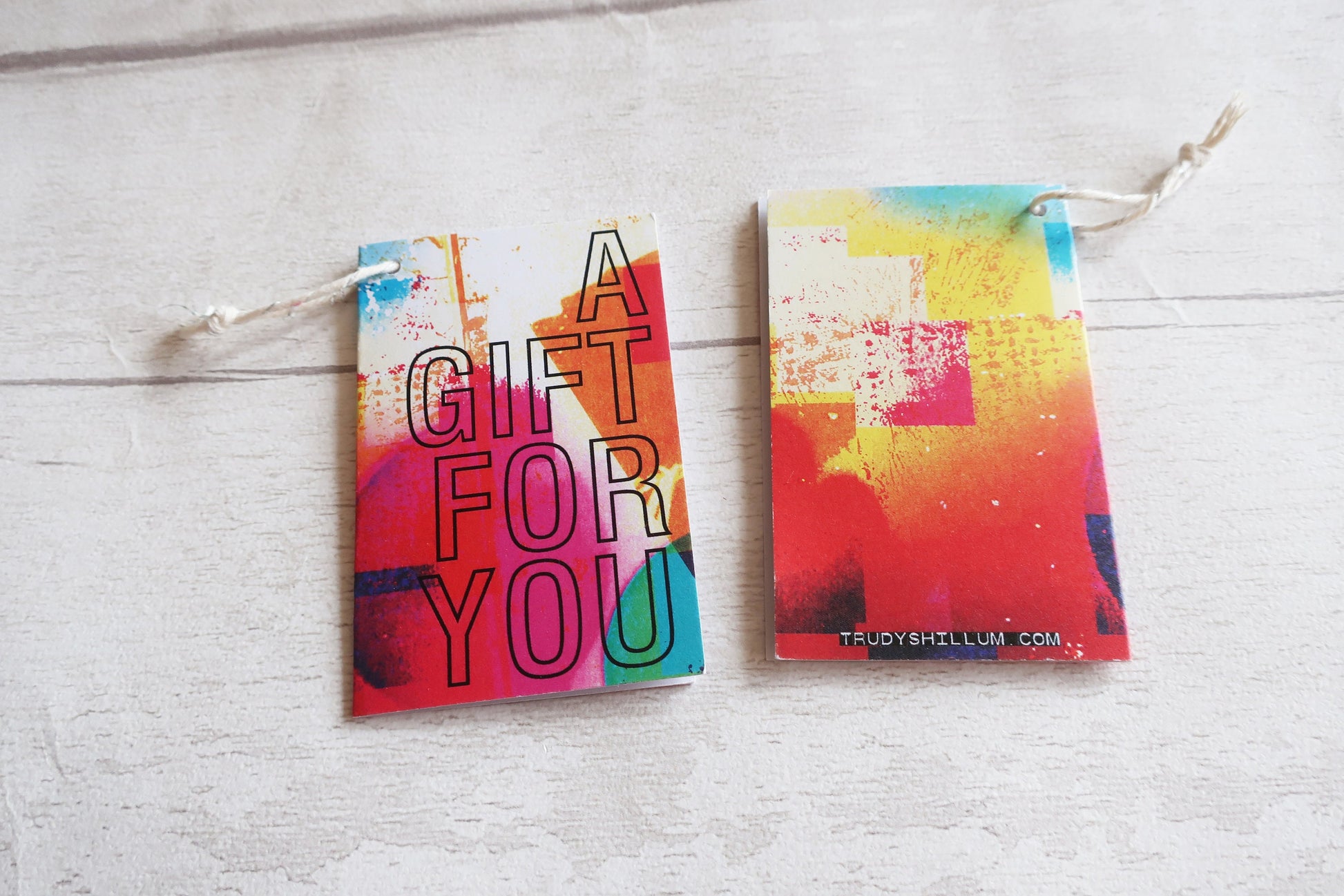 Two colorful gift tags with 'A Gift For You' text on a light wooden surface.