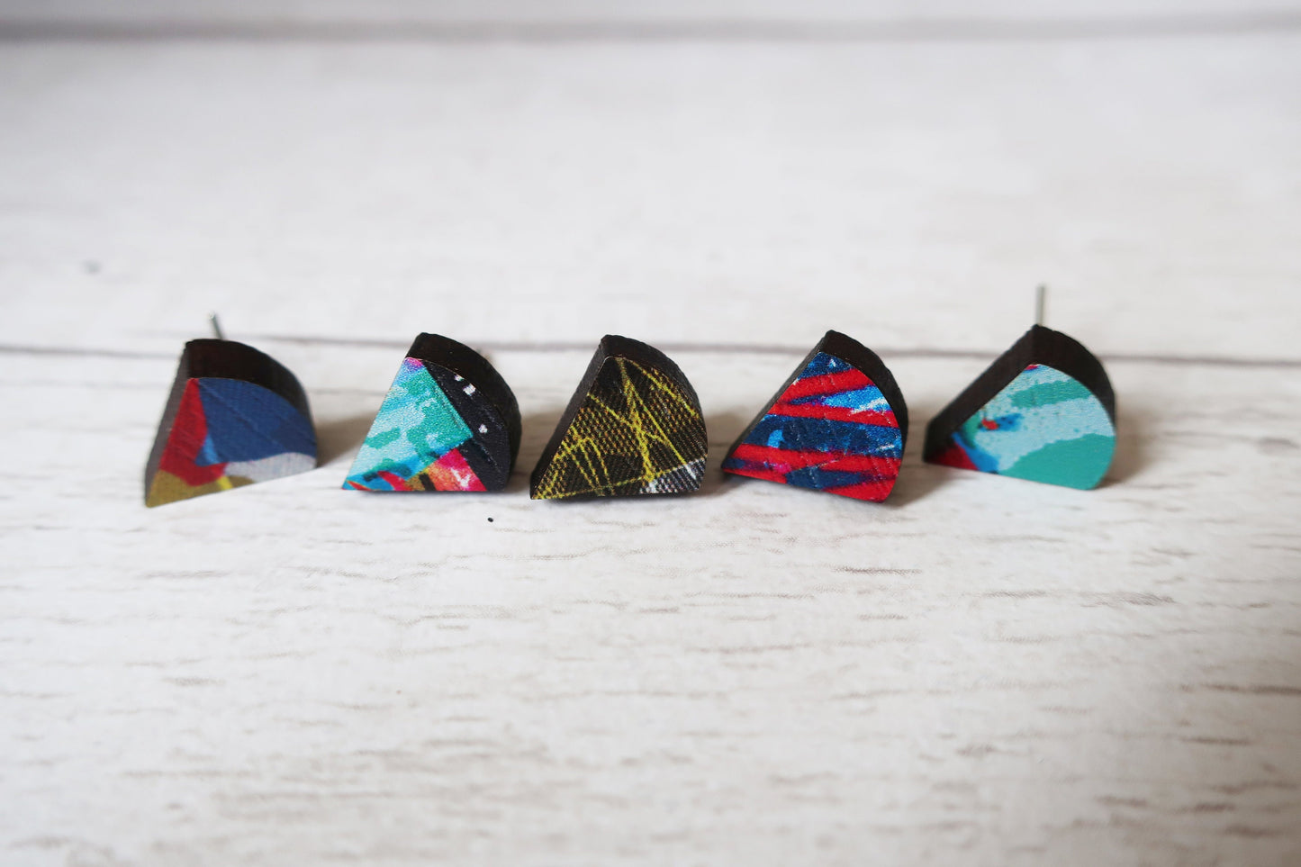Five colorful triangle-shaped earrings on a white surface