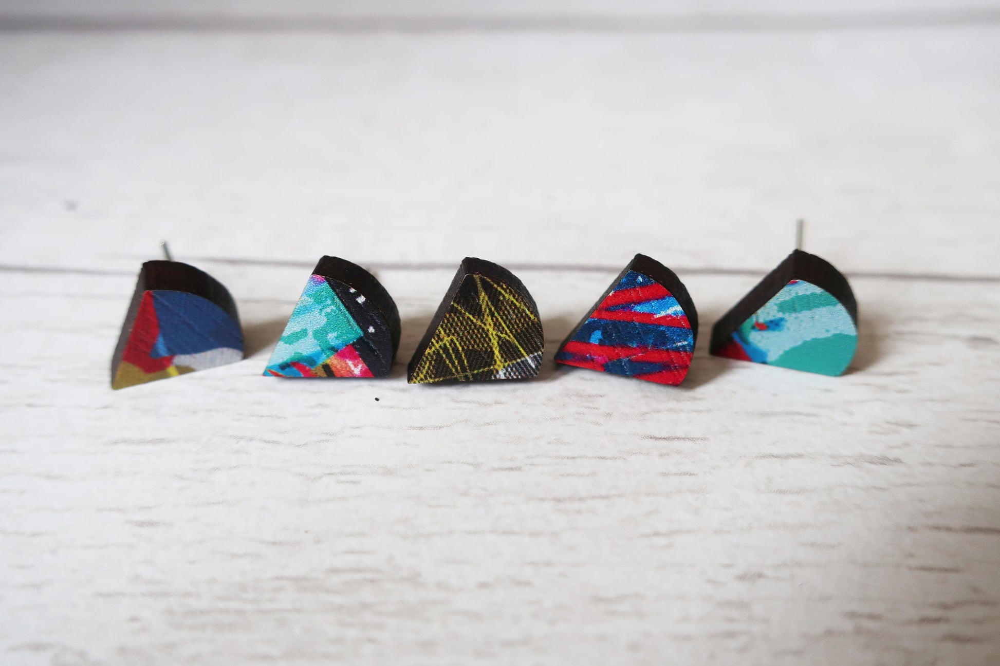 Five colorful triangle-shaped earrings on a white surface