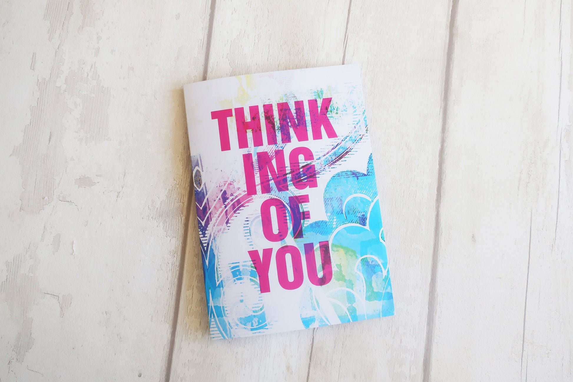 Greeting card with colorful design and 'Thinking of You' text on a light wooden surface