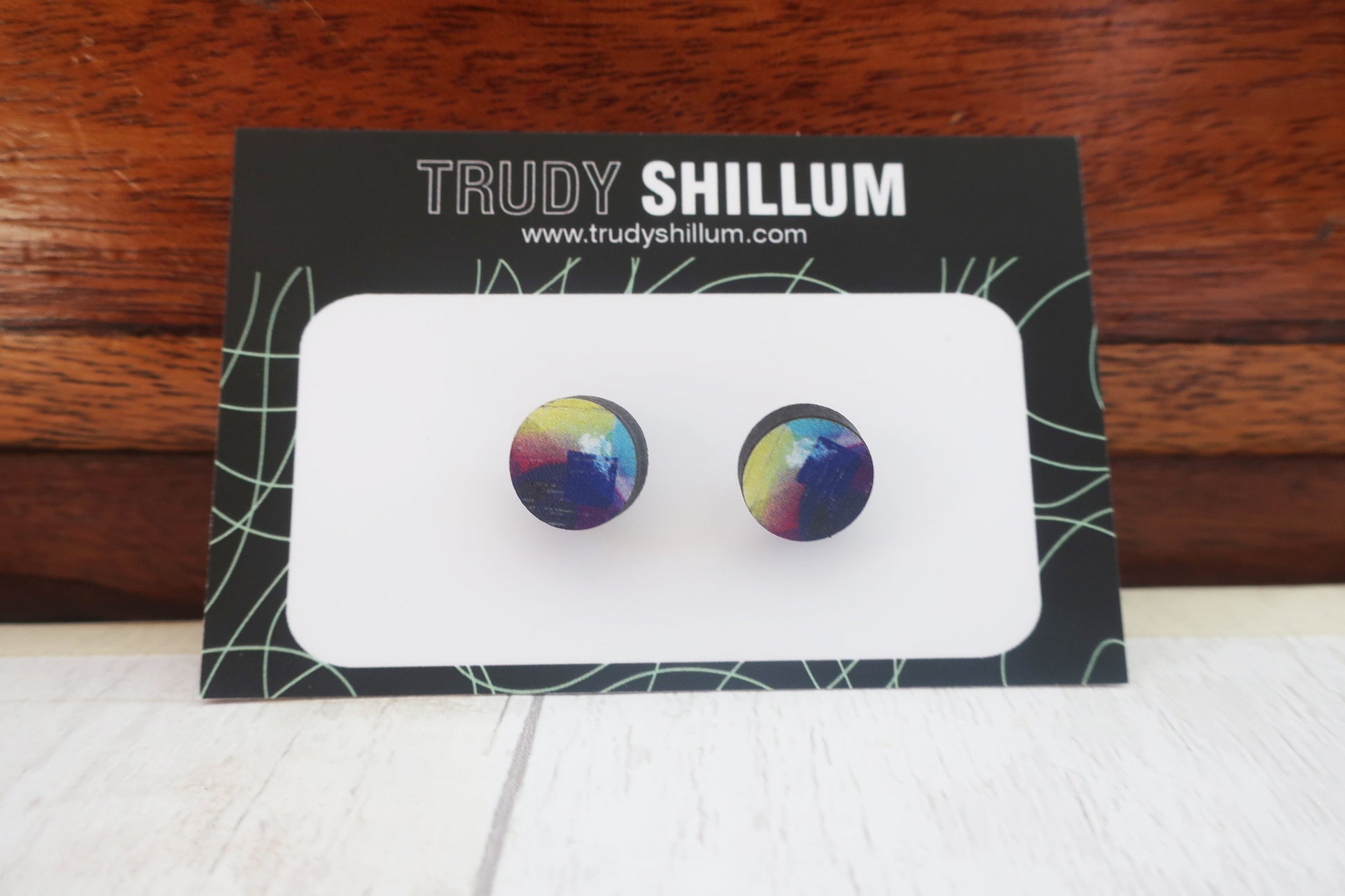 Colorful earrings on a Trudy Shillum branded card with a wooden background