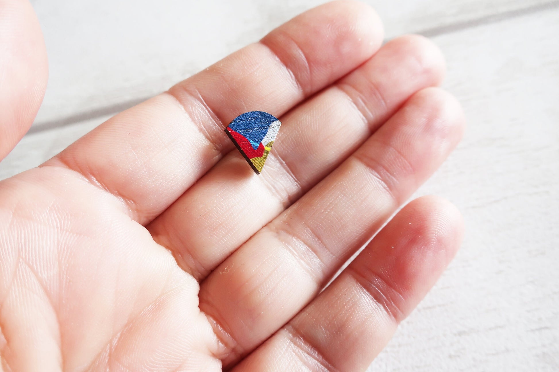 Colorful fan shaped earring held between fingers on a light background