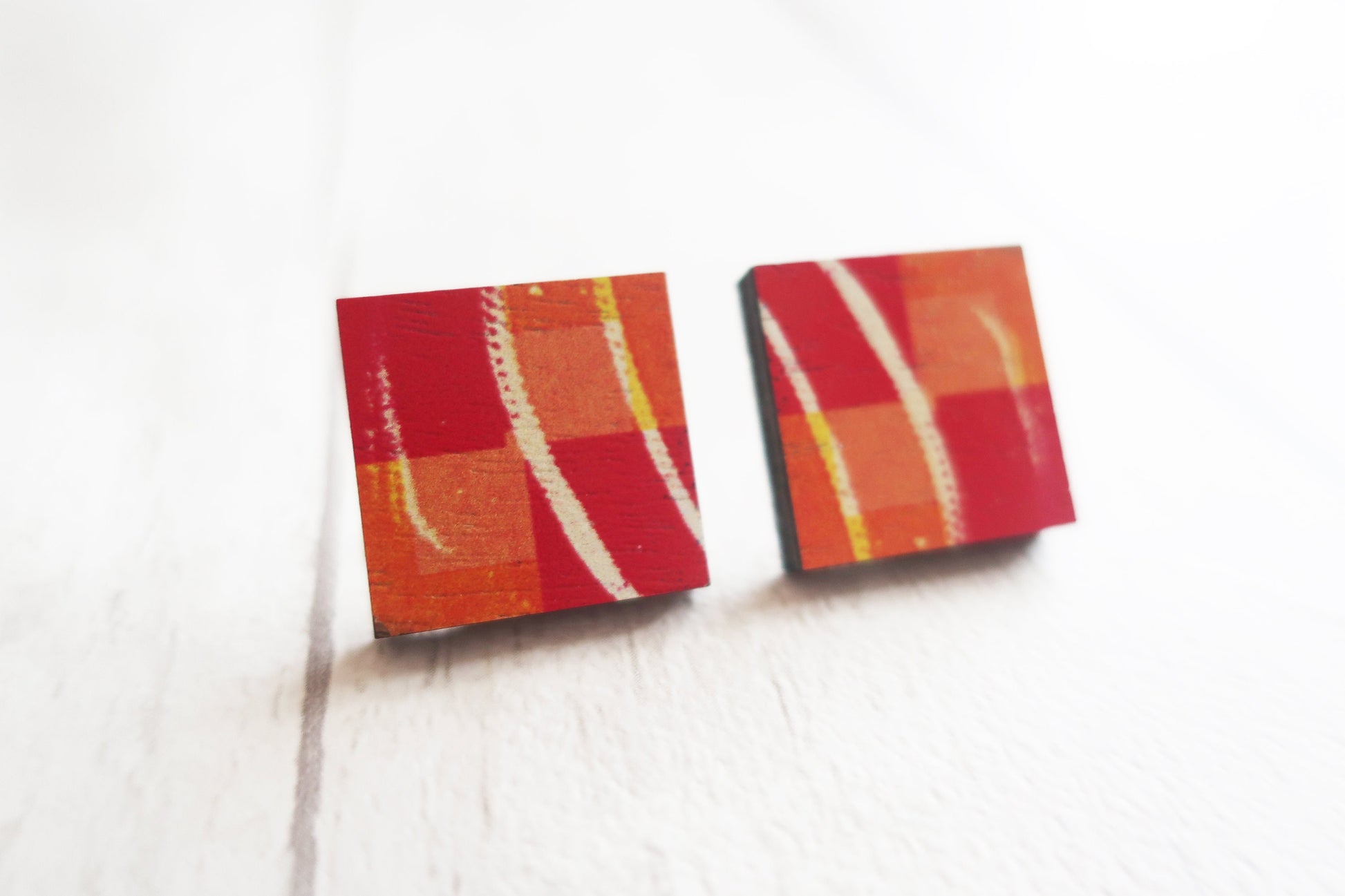Pair of square earrings with red and orange stripes on a white background