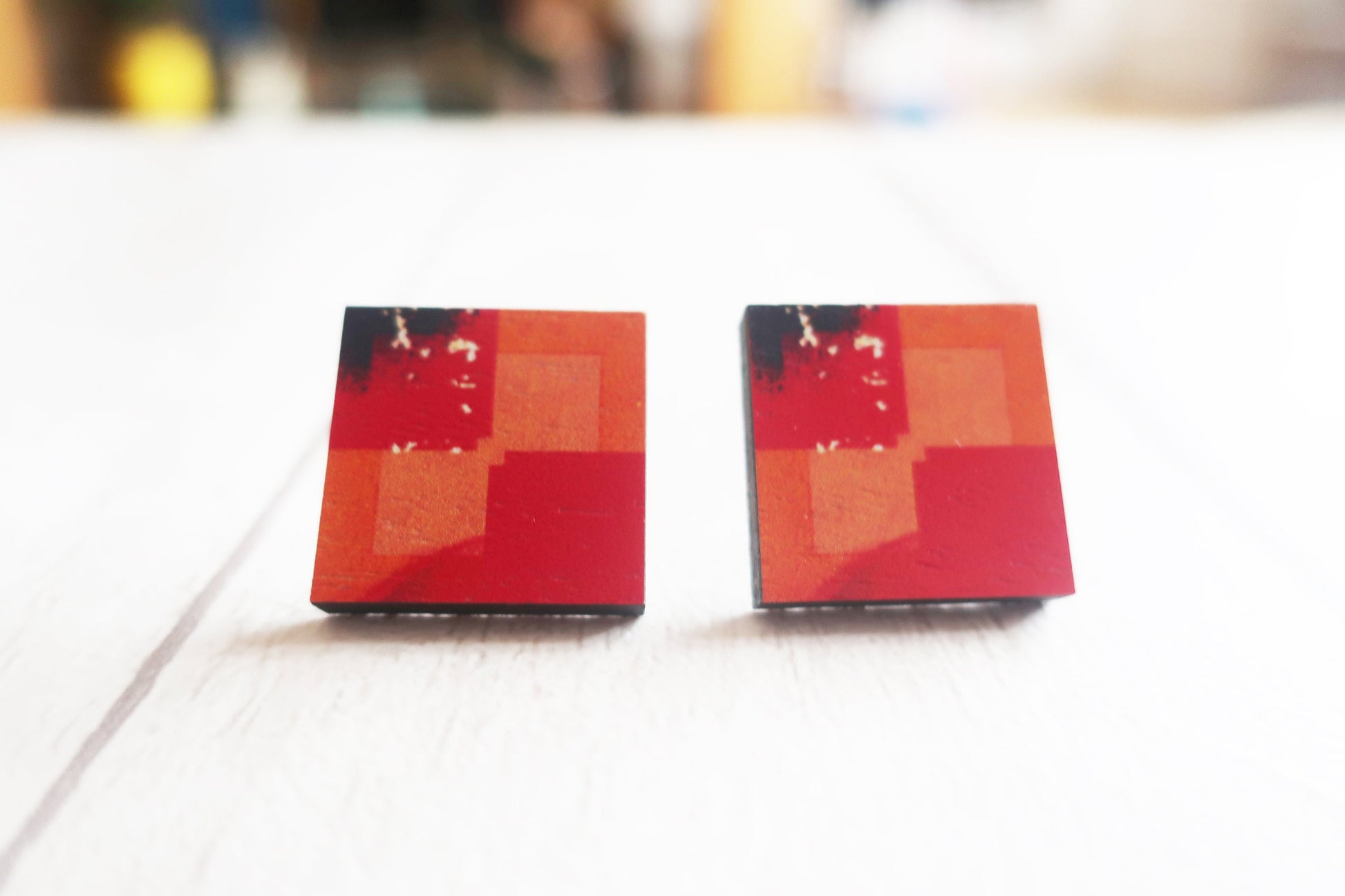 Pair of square-shaped earrings with red and orange pattern on a white surface