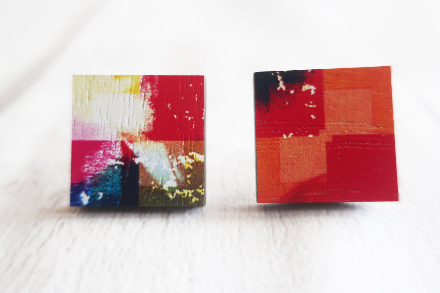 Two square earrings with abstract designs on a white surface