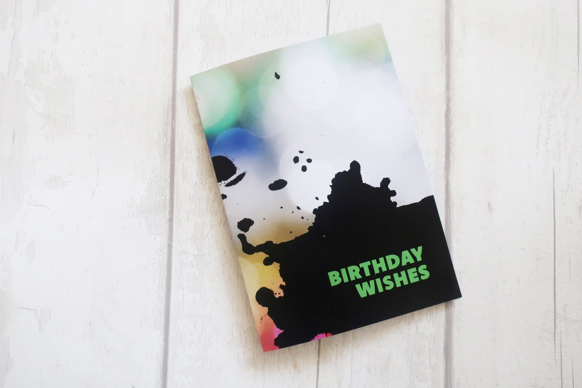 Greeting card with colorful design and 'Birthday Wishes' text on a white wooden surface