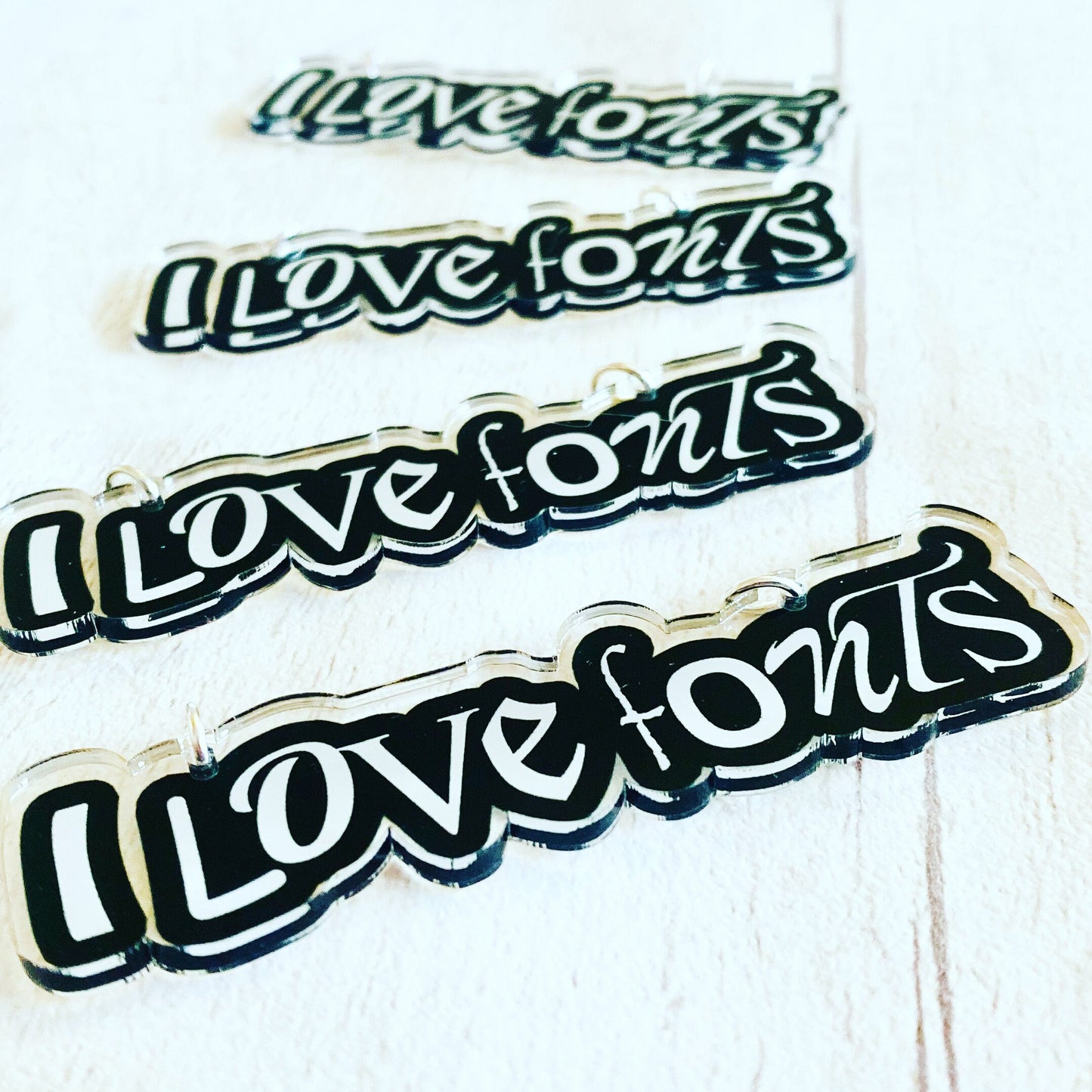 Four 'I love fonts' PENDANTS of different font styles on a white background