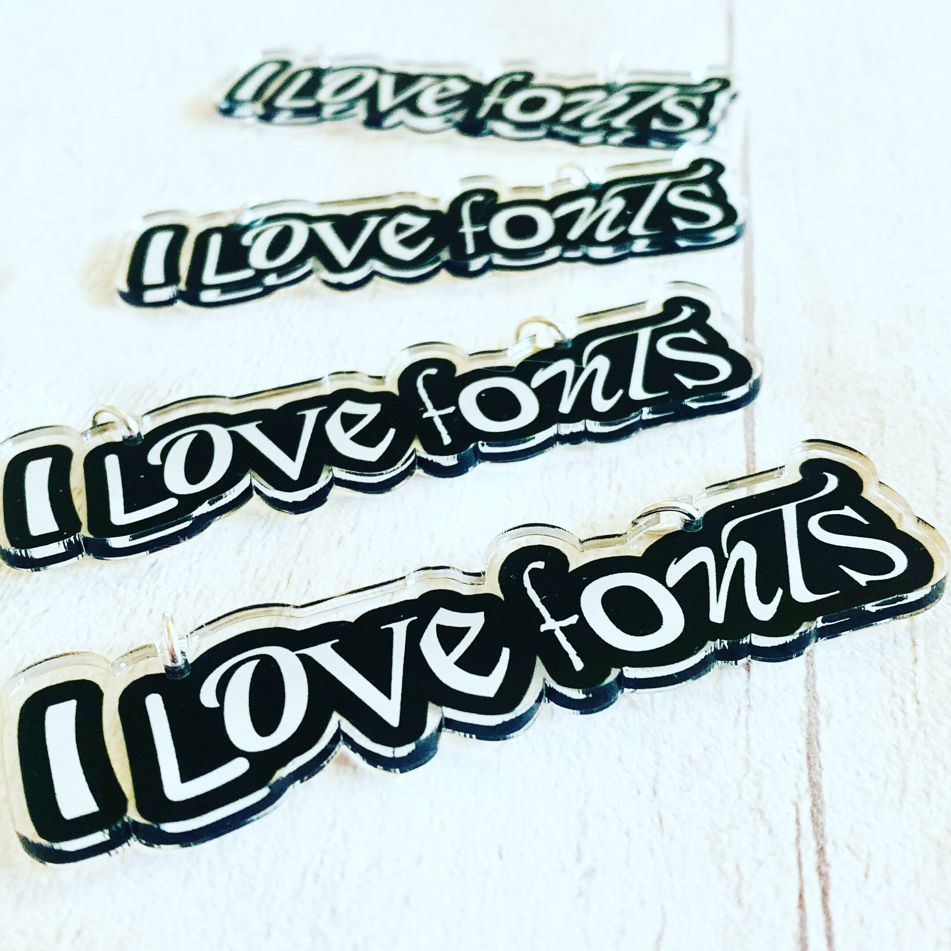 Four 'I love fonts' PENDANTS of different font styles on a white background