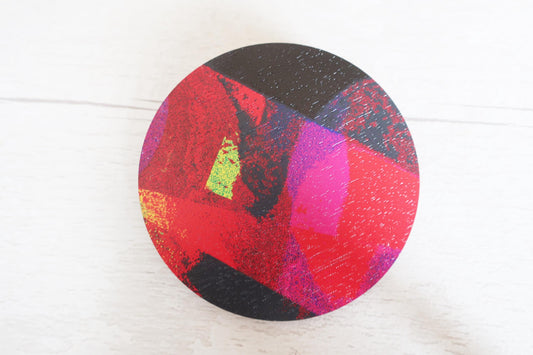 Round, multicolored brooch with black, red, pink, and green on a white background