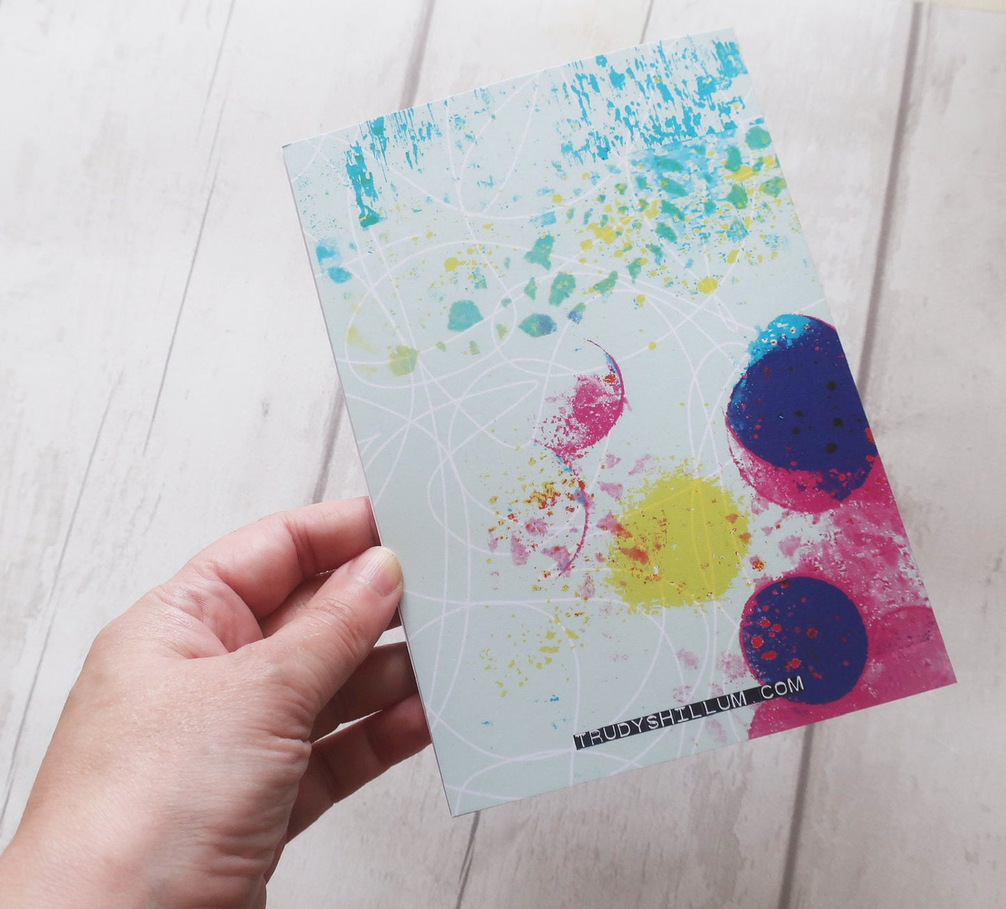 Hand holding a colorful splatter-patterned card on a light wooden surface