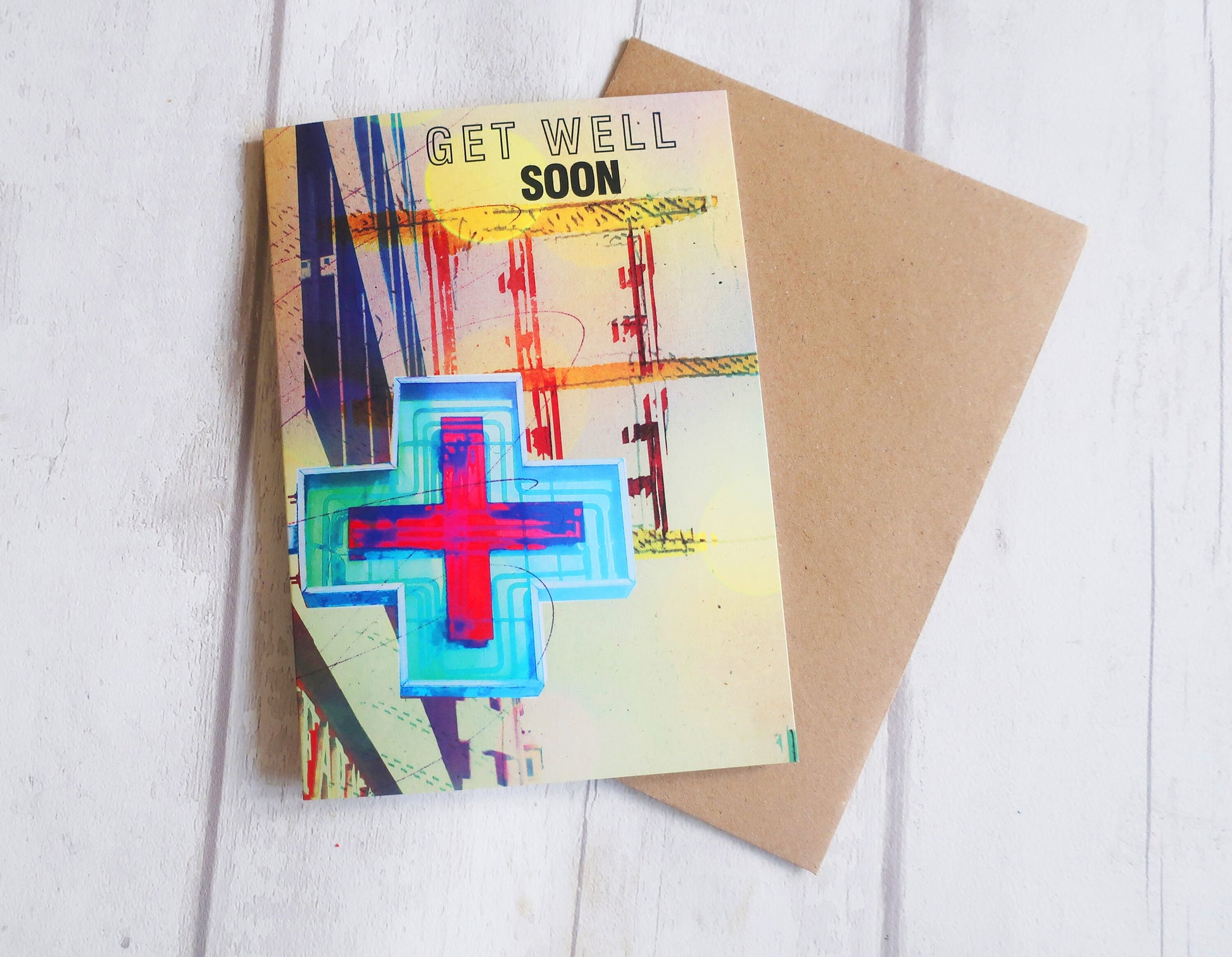 Colorful 'Get Well Soon' card with a red cross on a white wooden surface