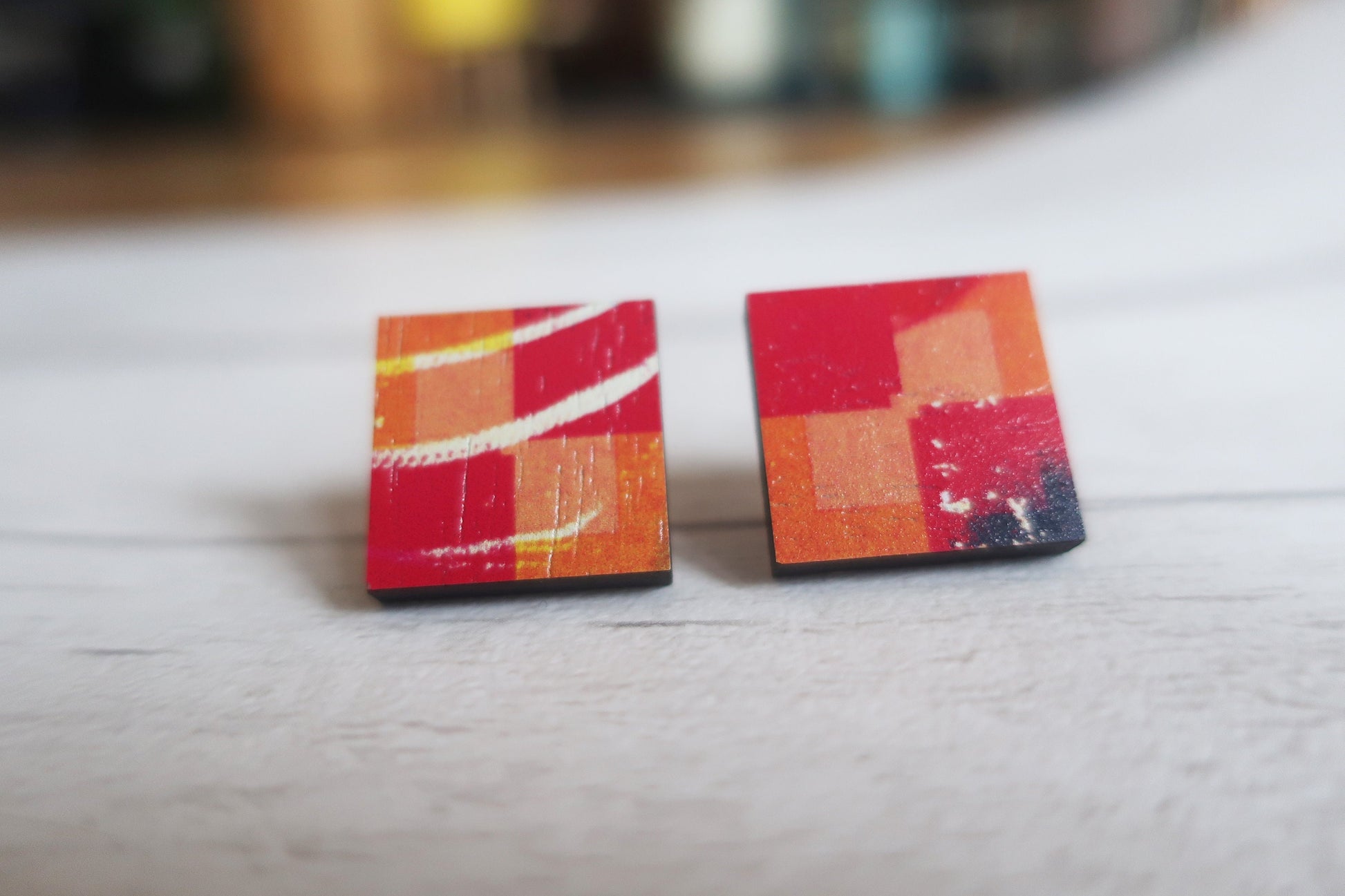 Pair of square earrings with colorful abstract design on a light surface.
