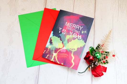 Colorful Christmas card with 'Merry Christmas' text, surrounded by red and green envelopes on a light wooden surface.