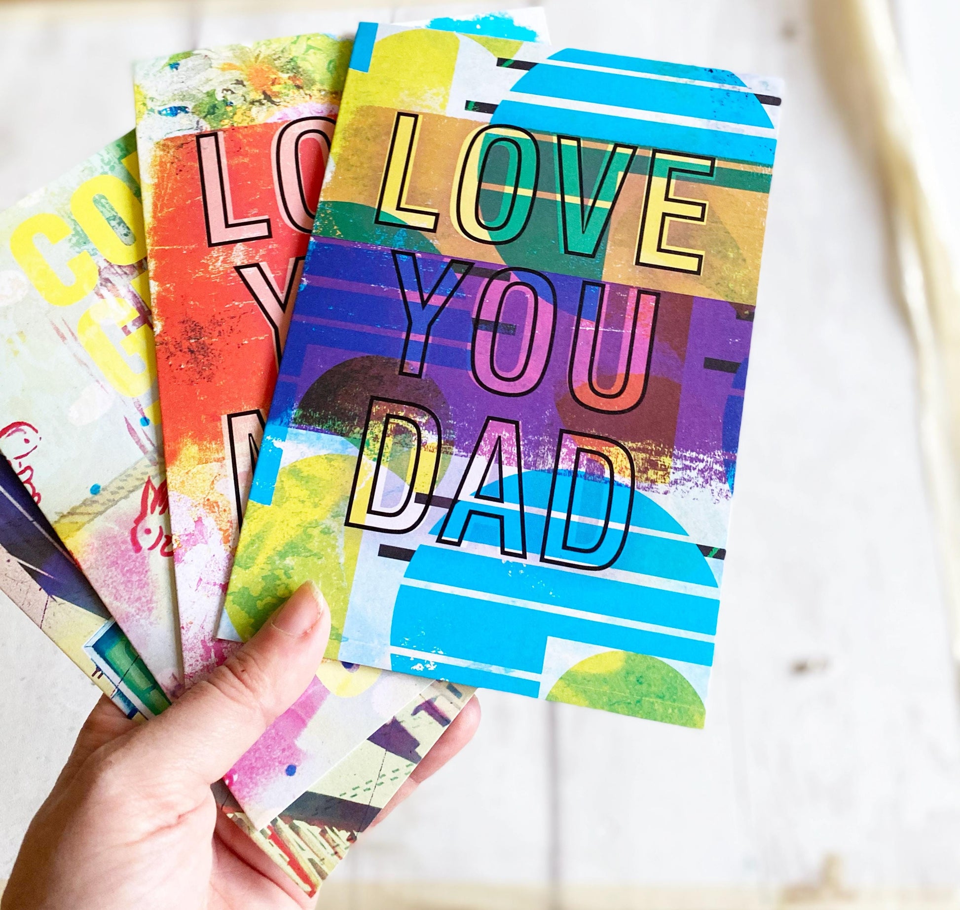 Colorful greeting cards with 'Love You Dad' text held by a hand on a light background