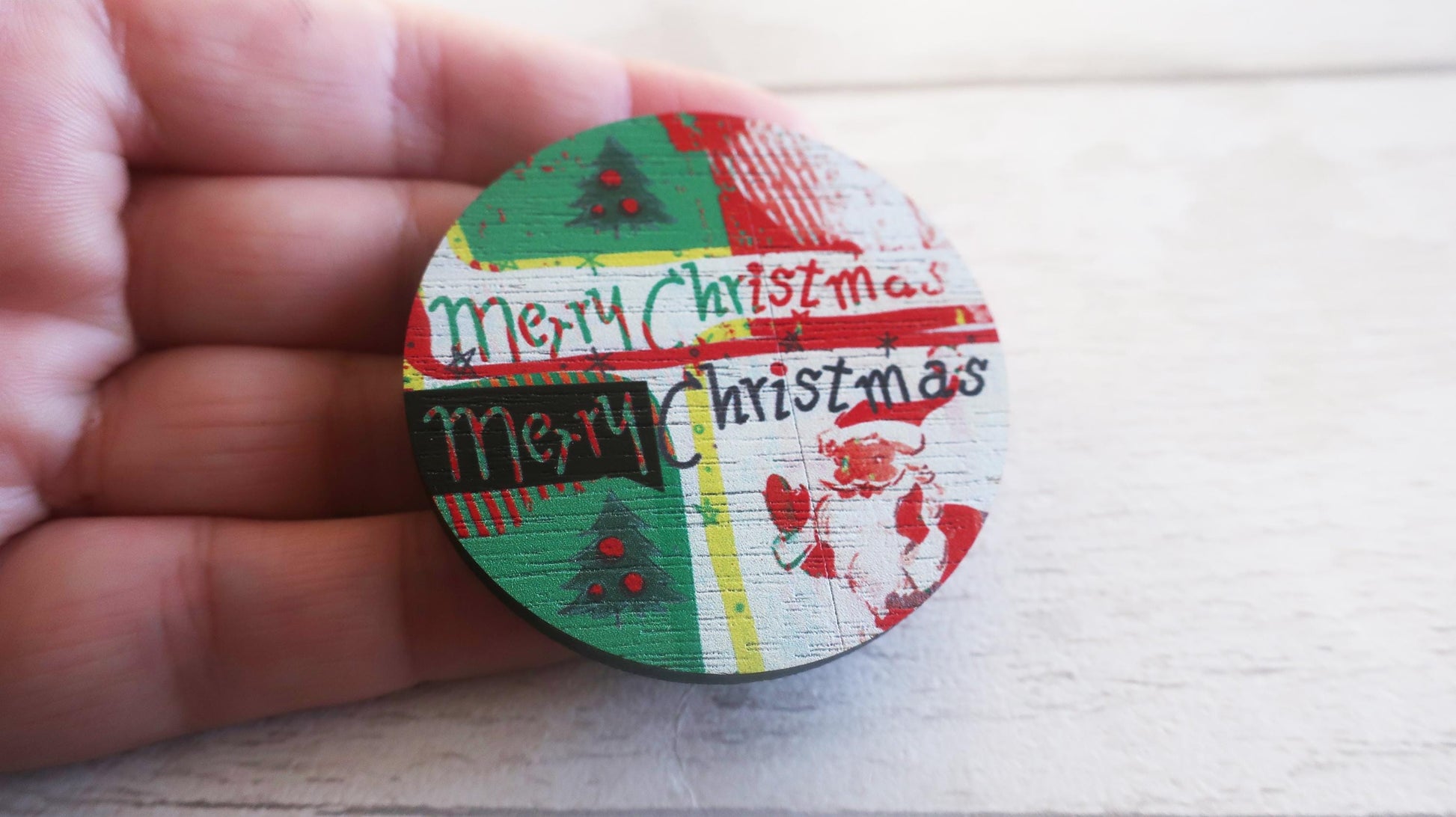 Round Christmas-themed badge held in a hand on a light wooden surface