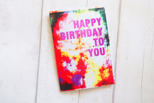 Colorful birthday card with 'Happy Birthday To You' text on a white wooden surface