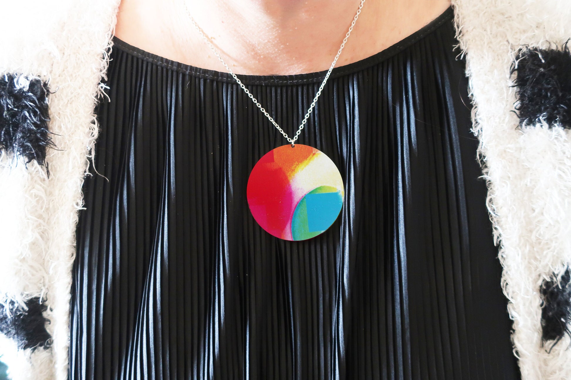 Person wearing a colorful circular pendant necklace with a black pleated dress.