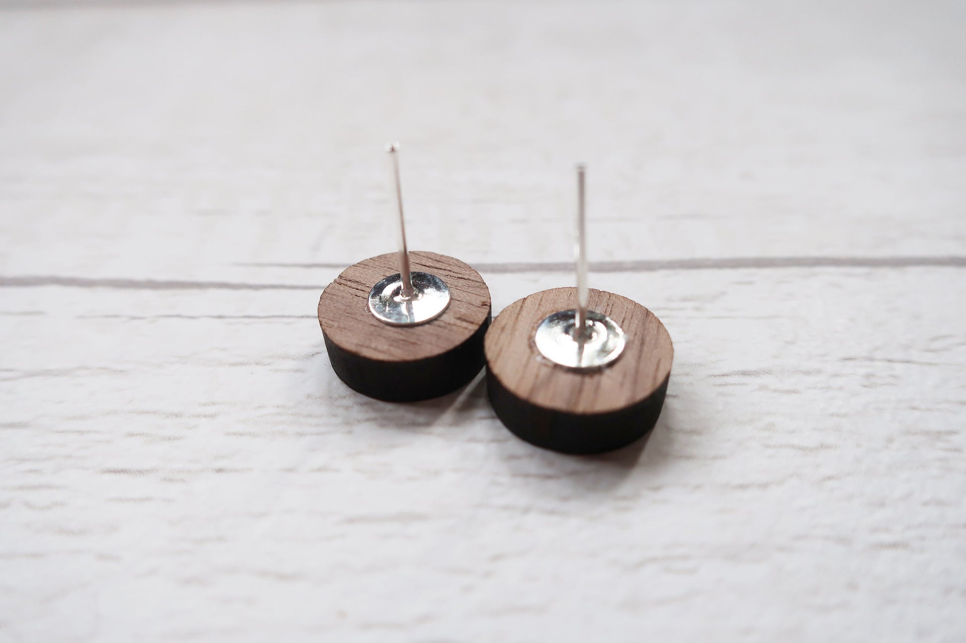 Two wooden earrings with metal components on a light wooden surface