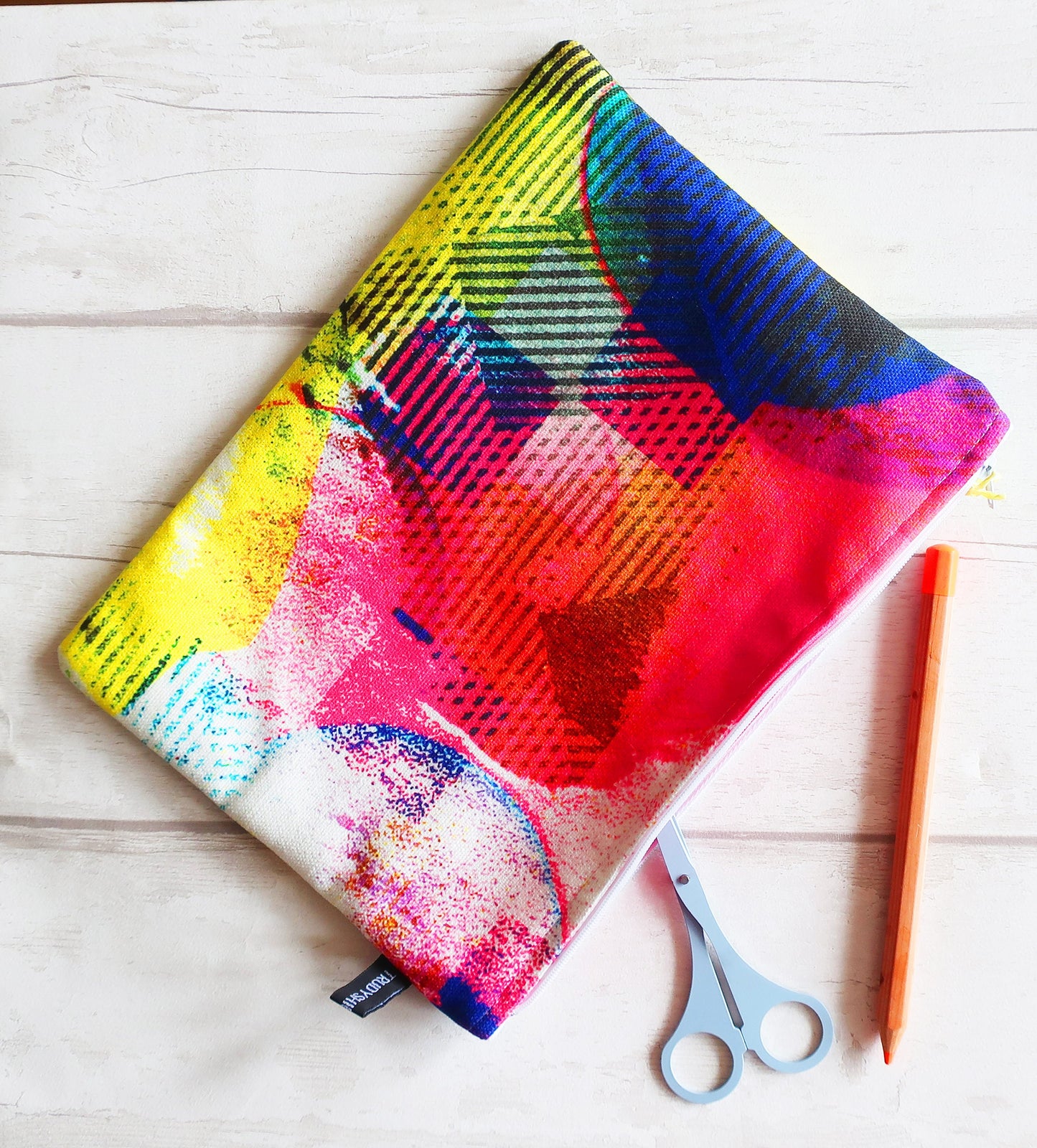 Colorful fabric pouch with abstract patterns on a wooden surface with scissors and a pencil.