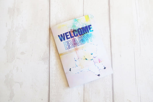 Colorful greeting card with 'Welcome Baby' text on a light wooden surface