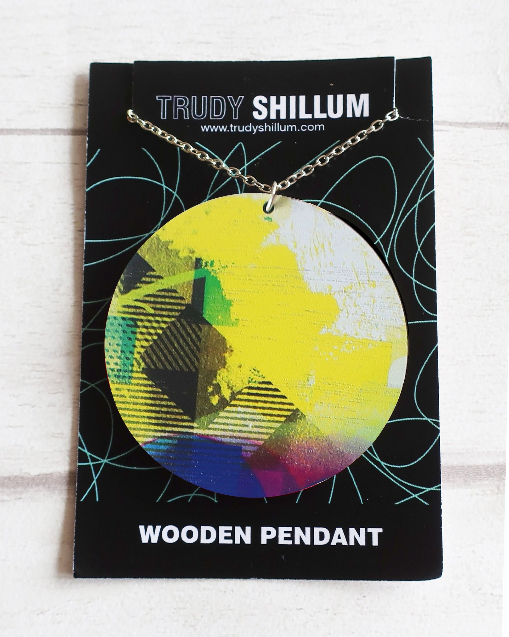 Colorful wooden pendant on a Trudy Shillum branded card with a white background