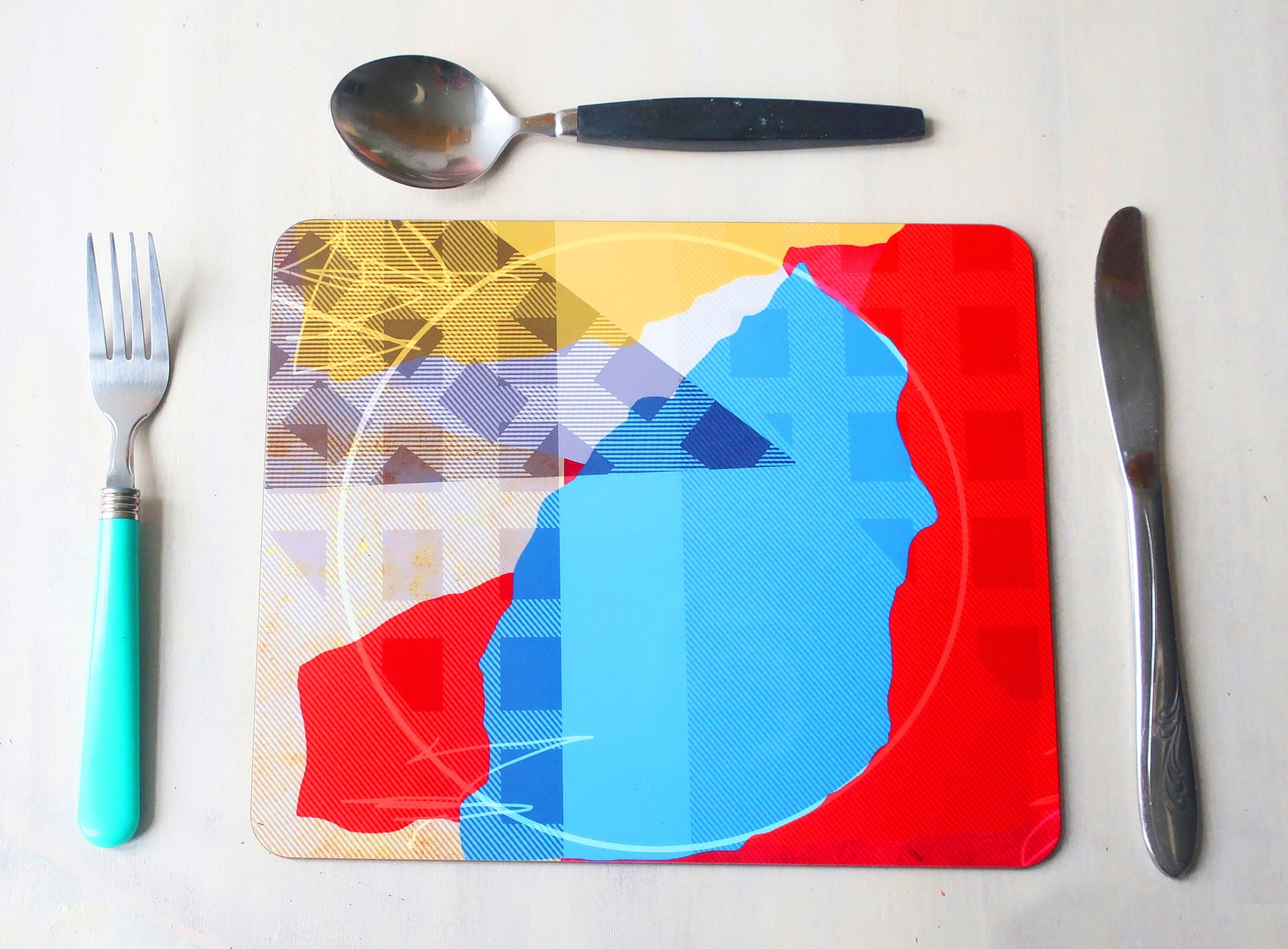 Colorful abstract design on a placemat with fork, knife, and spoon on a white background