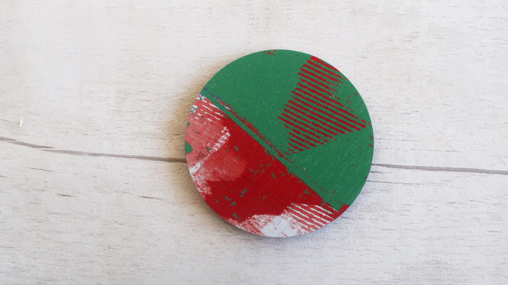 Circular brooch with red and green design on a light wooden surface