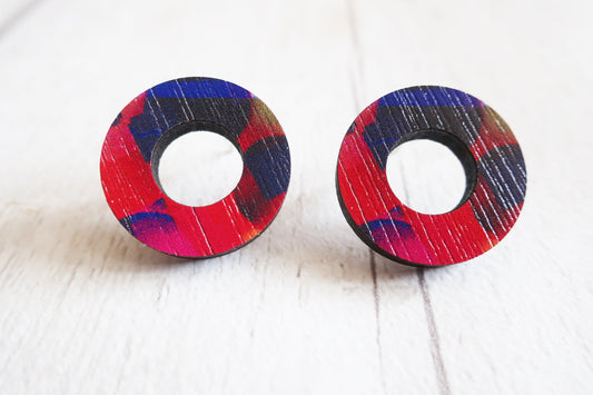 Pair of round earrings with colorful design on a white wooden surface