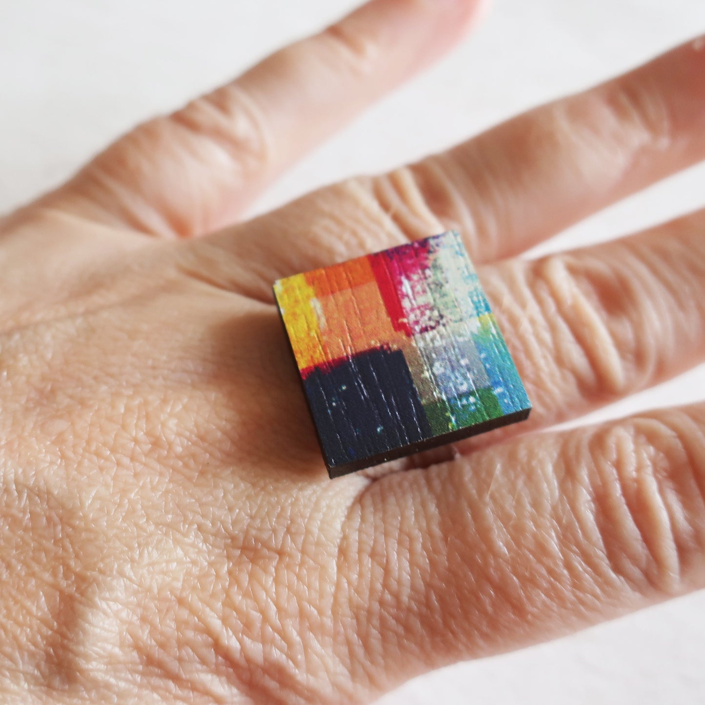 Colorful square ring on a person's finger with a white background