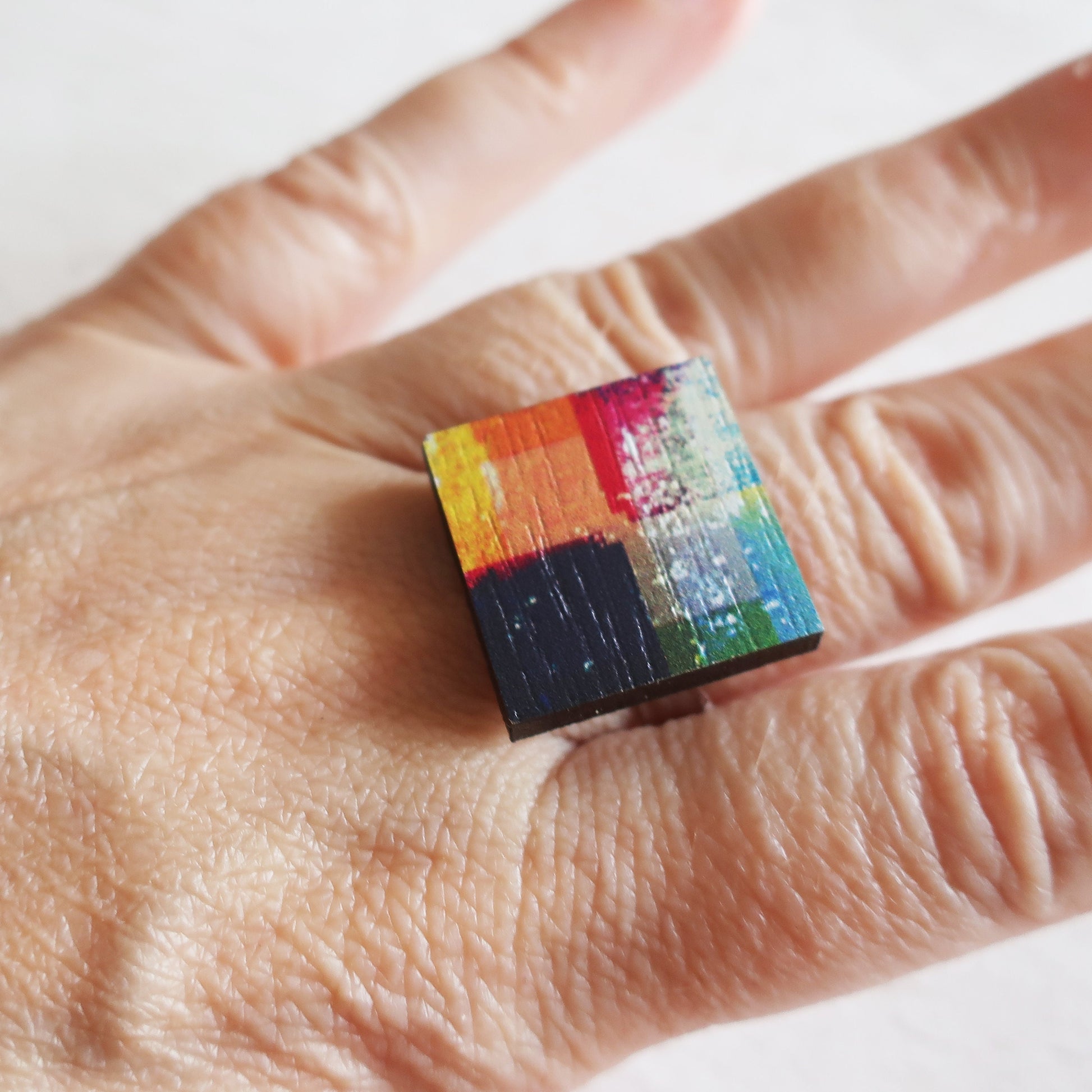 Colorful square ring on a person's finger with a white background
