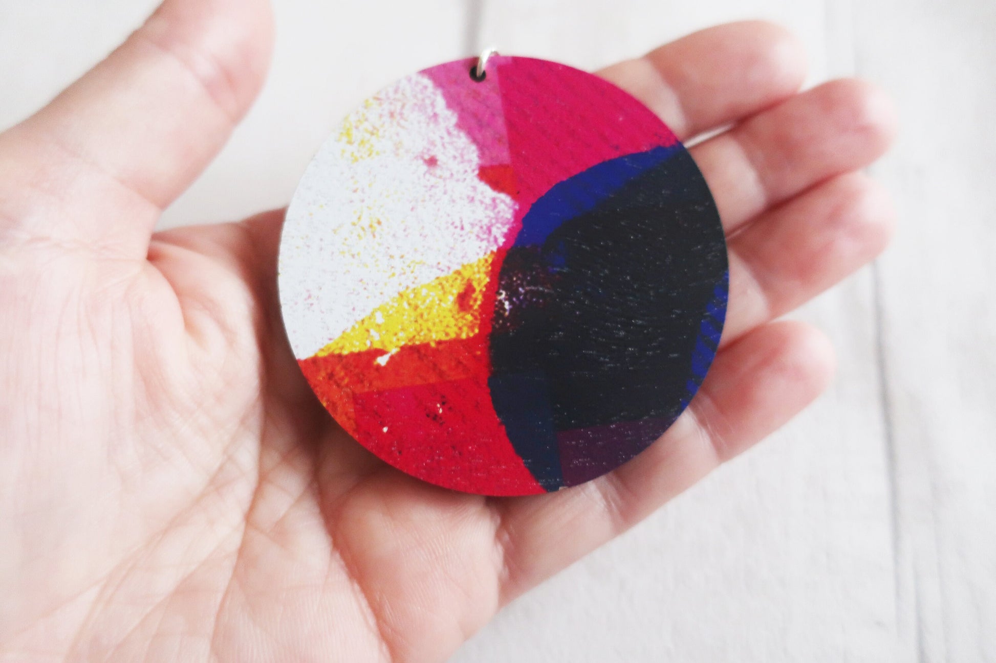 Colorful circular necklace held in a hand against a white background