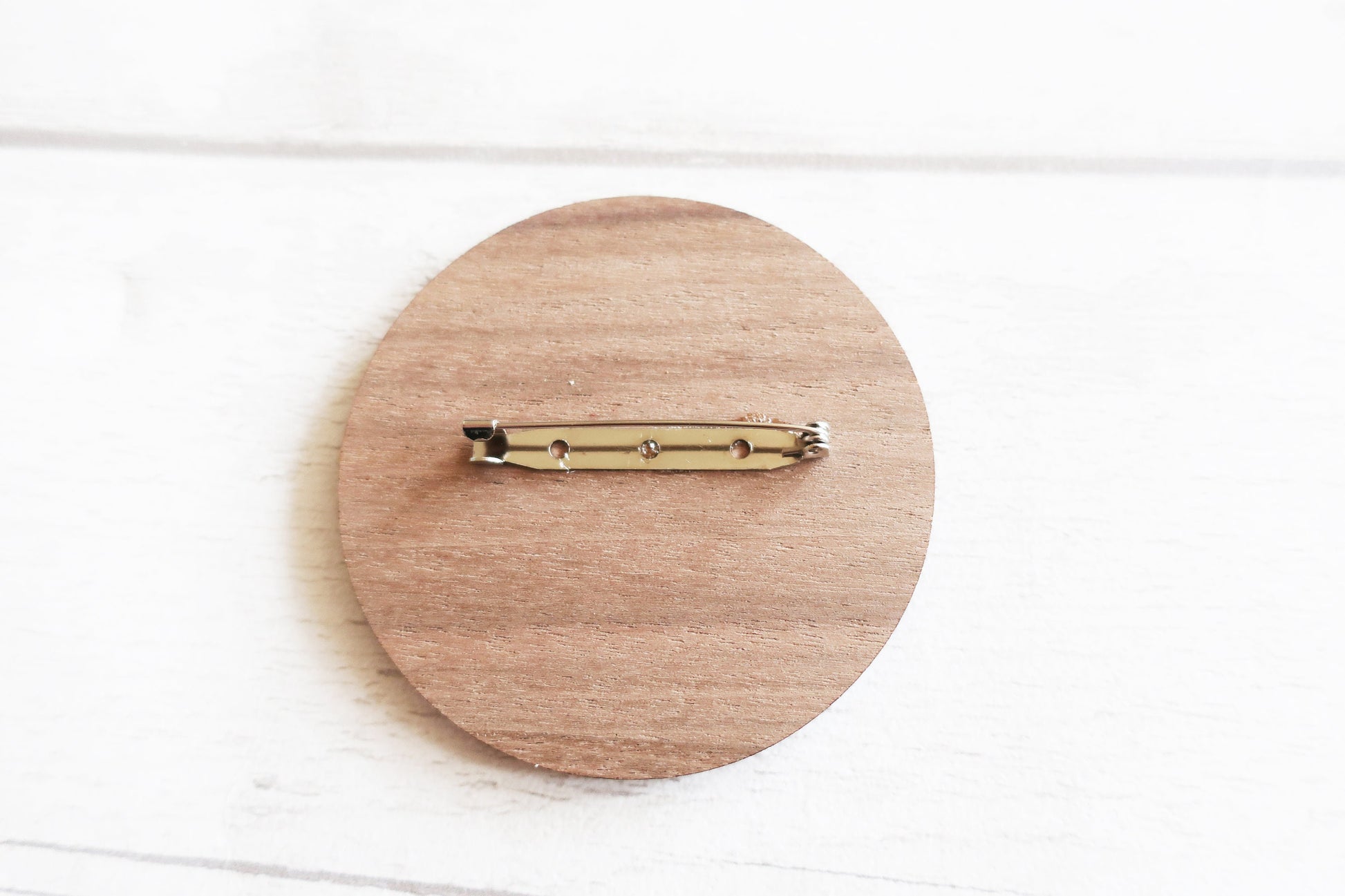 Wooden circular brooch with a gold clip on a white background