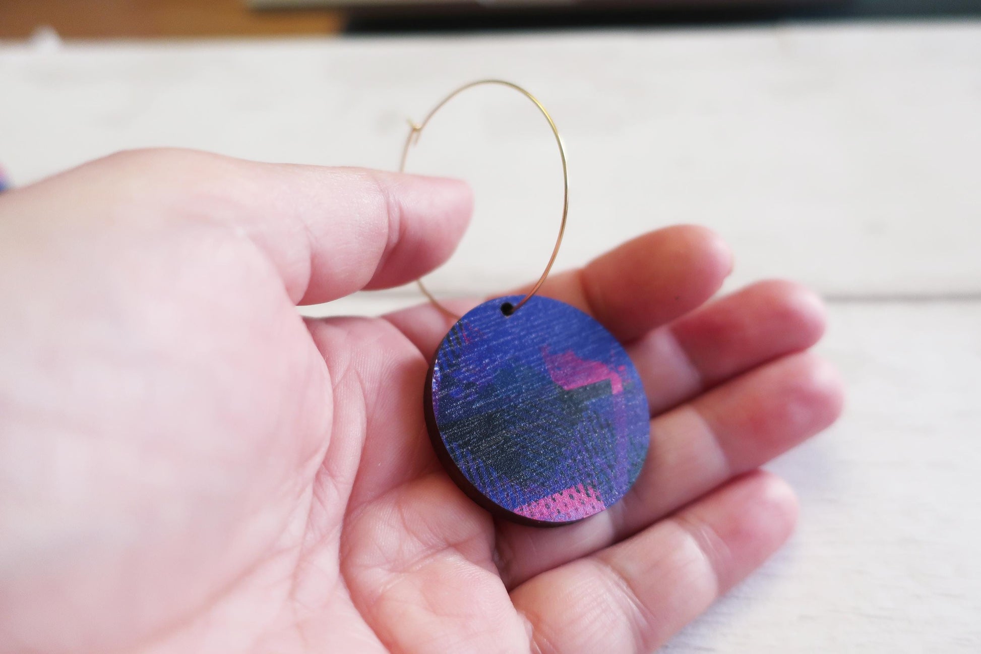 Hand holding a colorful oval earring with a blurred background