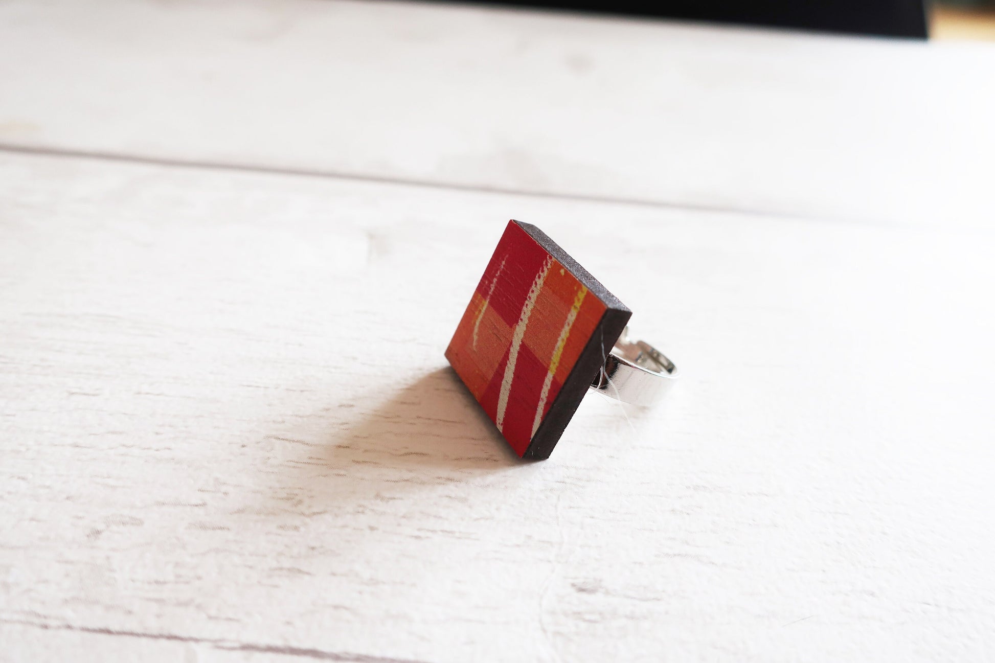 Square ring with red and gold design on a white wooden surface