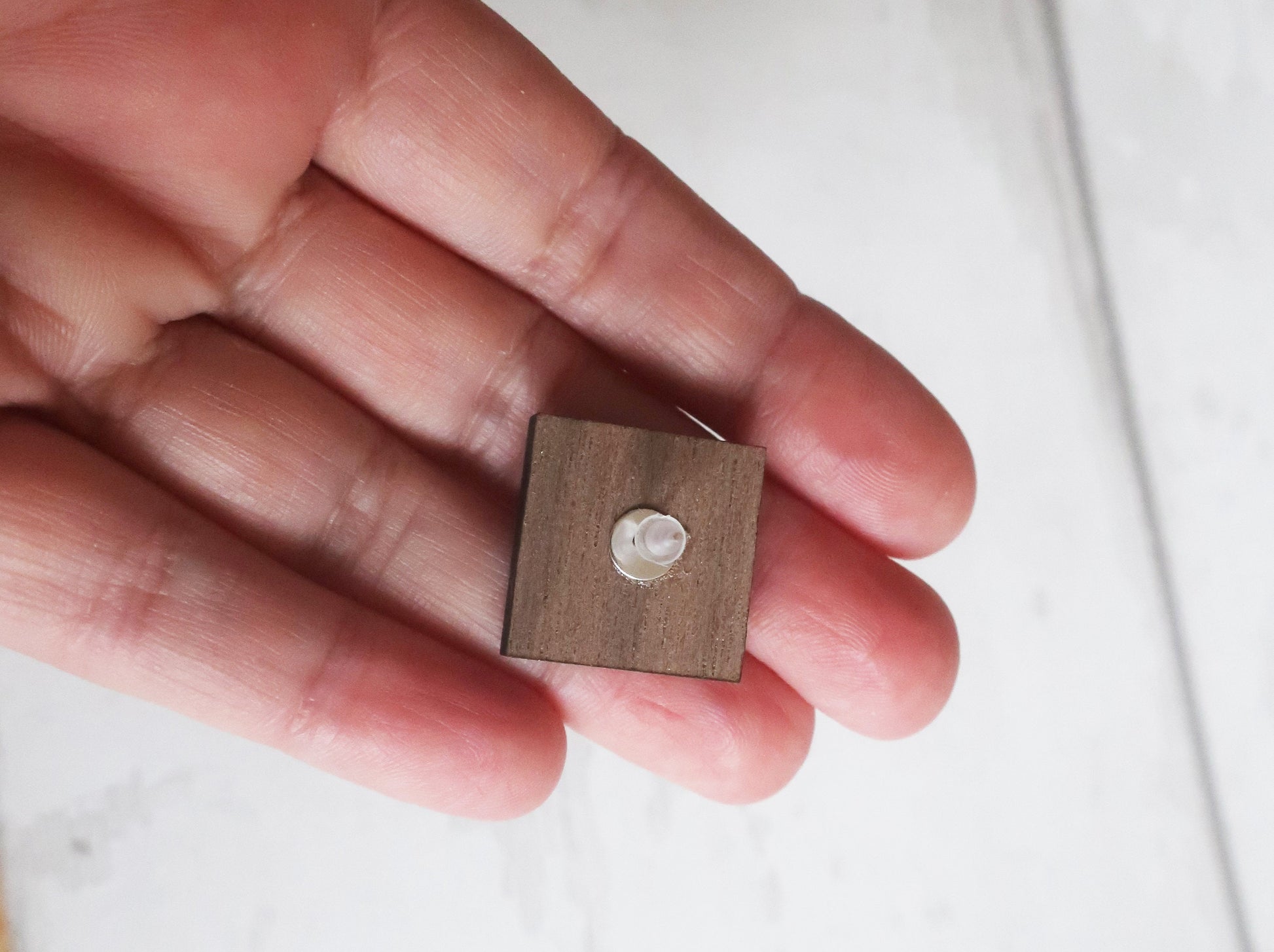 Wooden earring back held between fingers on a light background