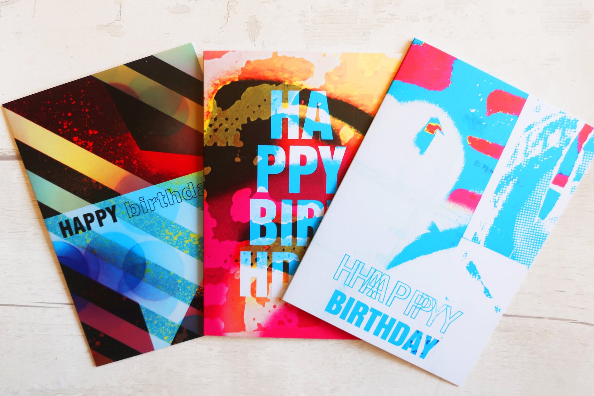 Three colorful birthday cards with 'Happy Birthday' text on a light wooden surface.