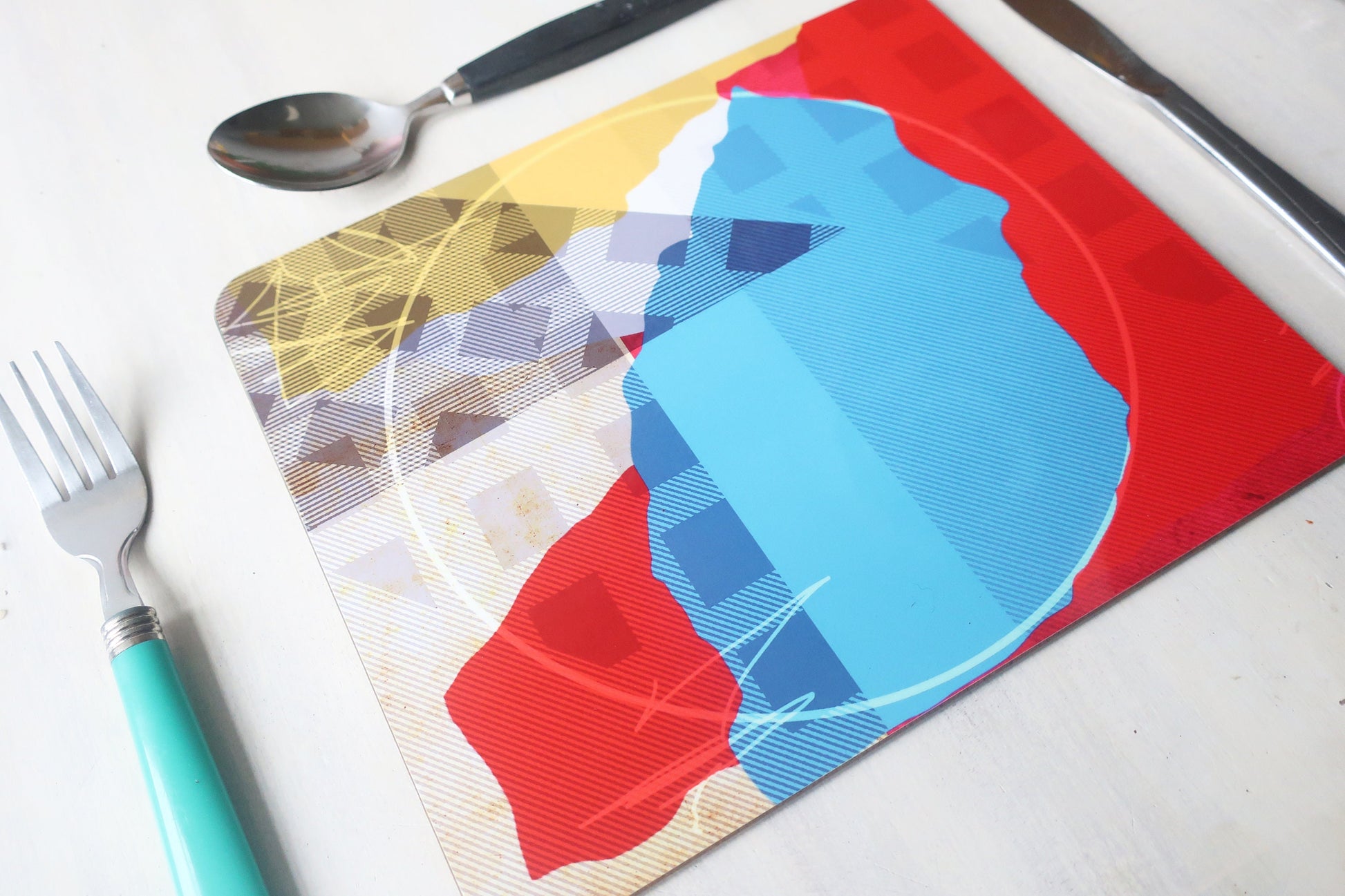 Colorful placemats with geometric patterns on a white surface with cutlery.