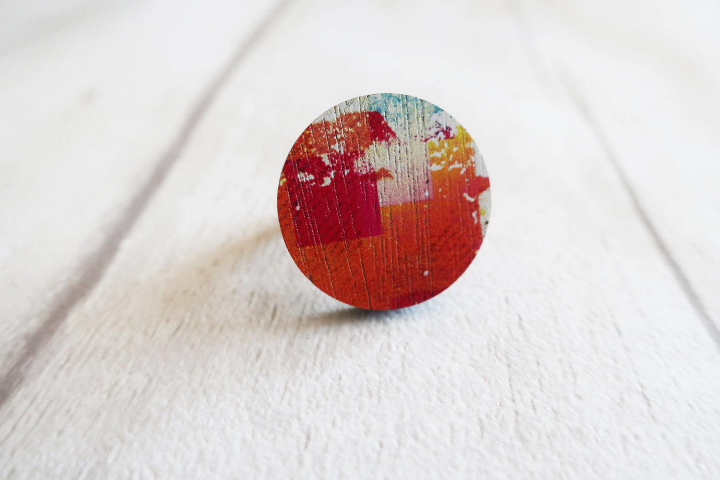Round wooden ring with multicolored design on a white fabric background