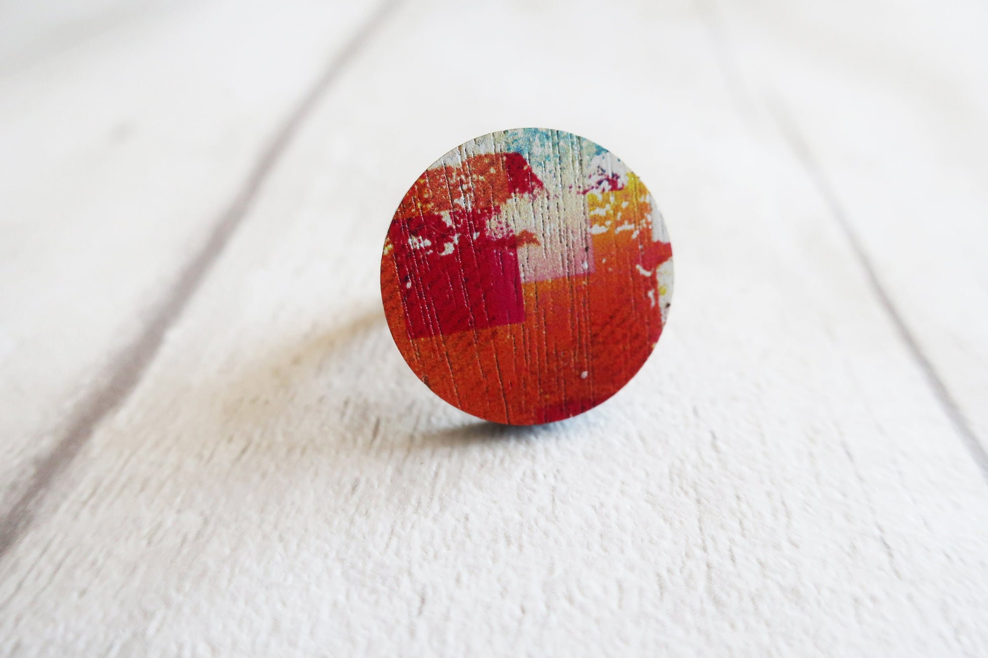 Round wooden ring with multicolored design on a white fabric background