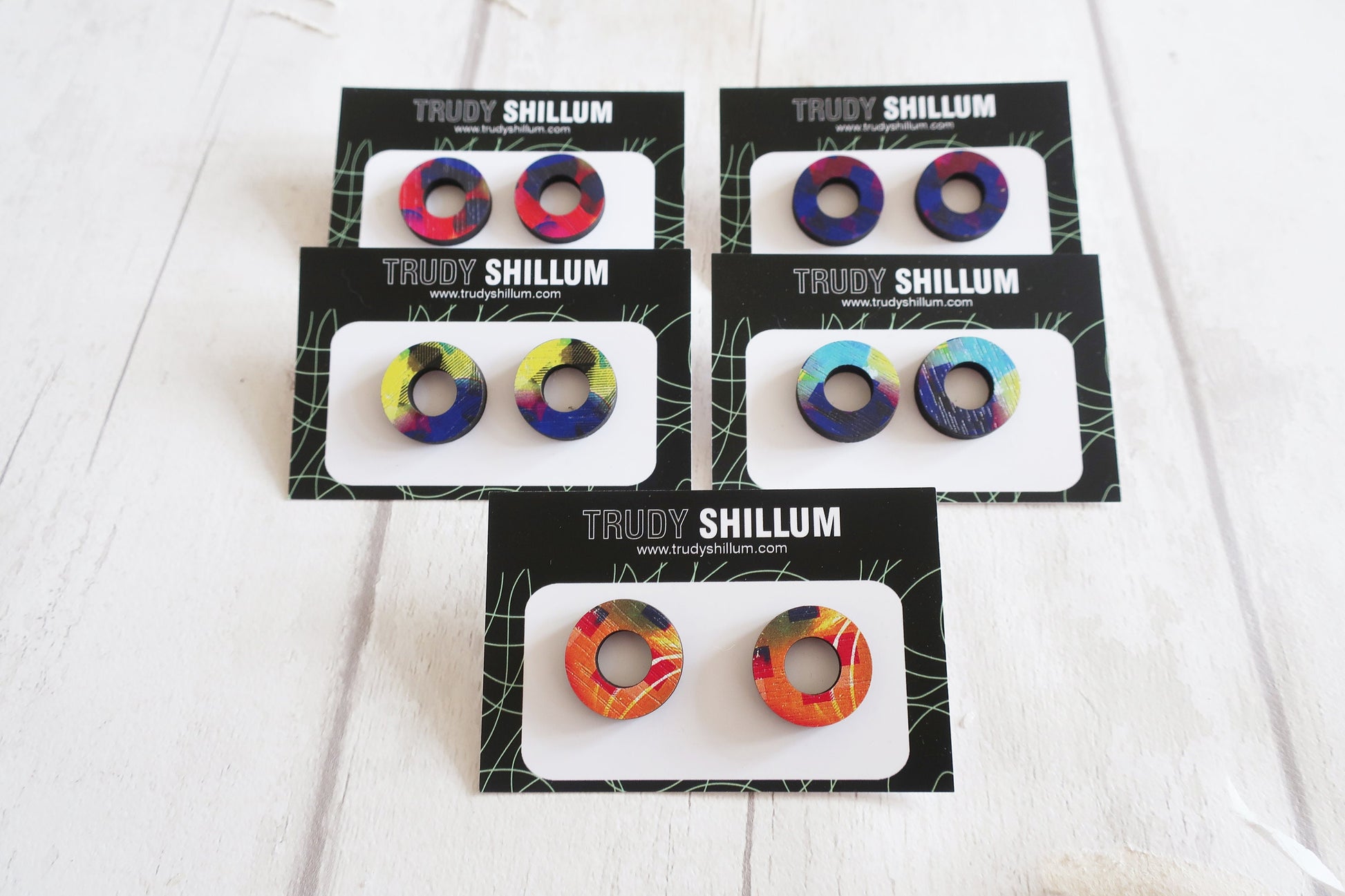 Set of colorful earrings on display with Trudy Shillum packaging on a white background