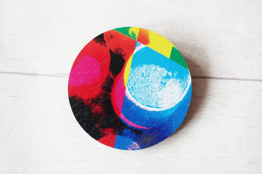 Colorful circular brooch with abstract design on a white wooden surface