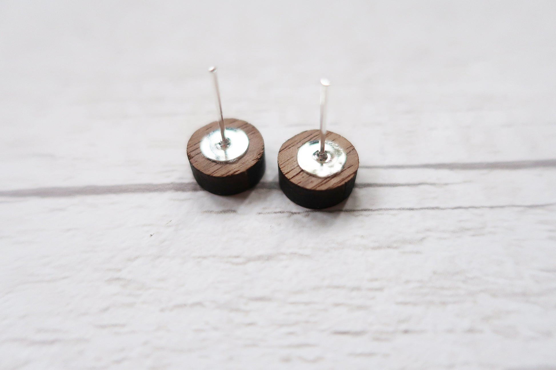 Pair of wooden earrings with silver tops on a light wooden surface