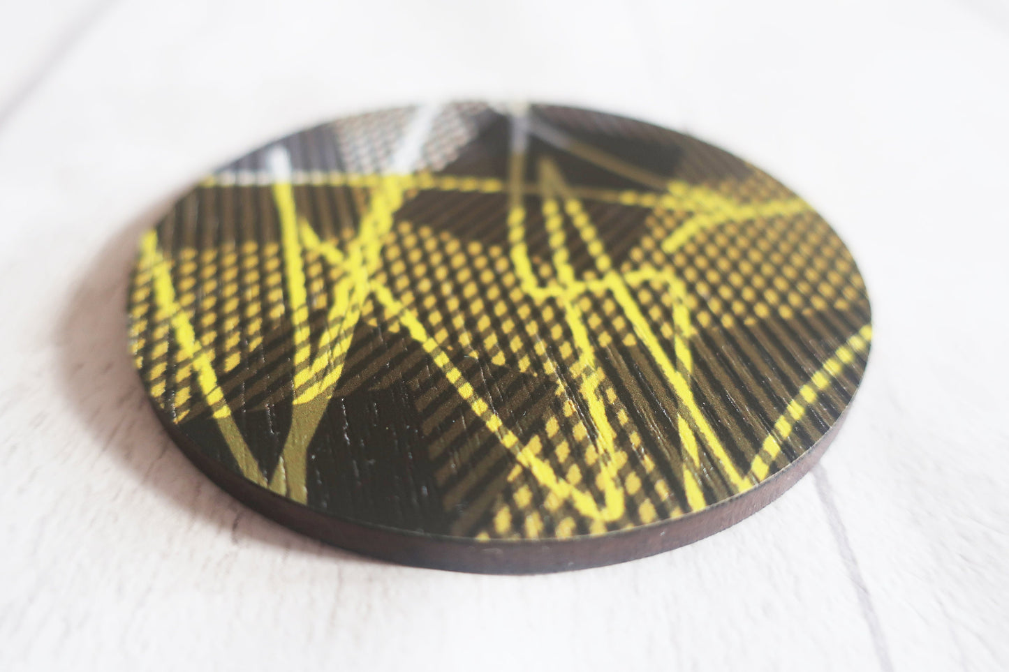 Round black and yellow patterned brooch on a white background