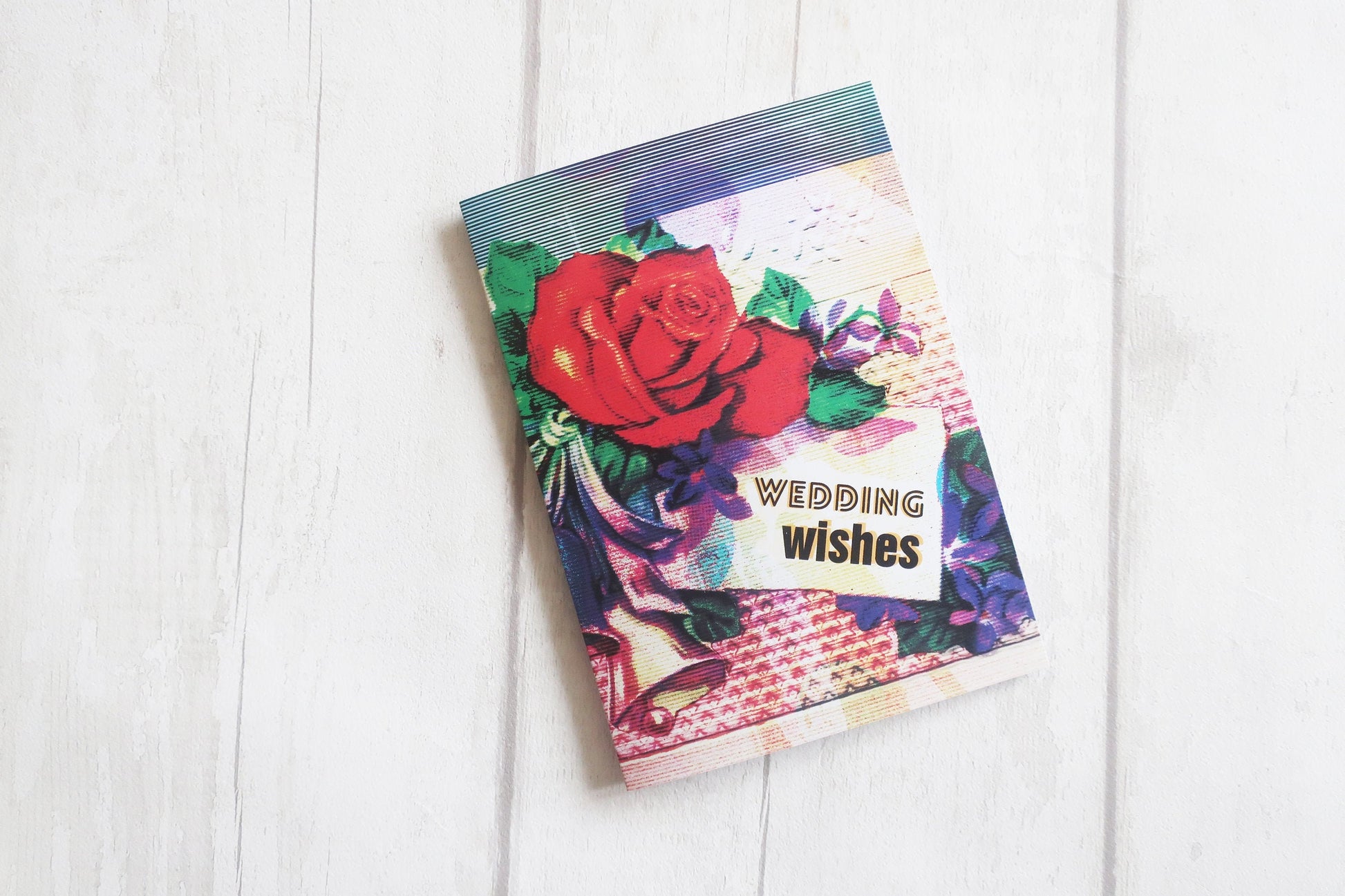 Colorful card with floral design and 'Wedding Wishes' text on a white wooden surface