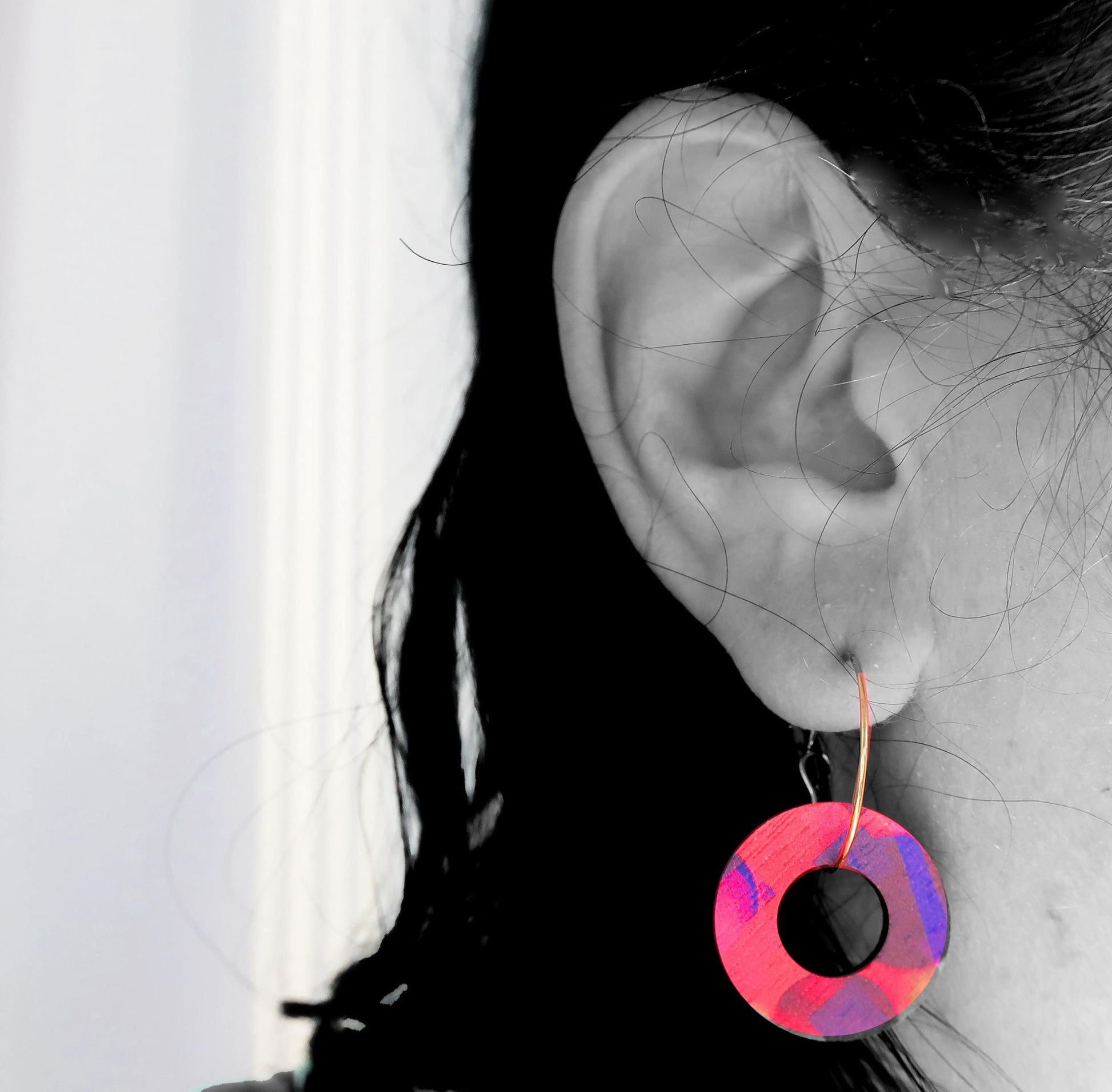 Close-up of an ear wearing a colorful hoop earring with a blurred background