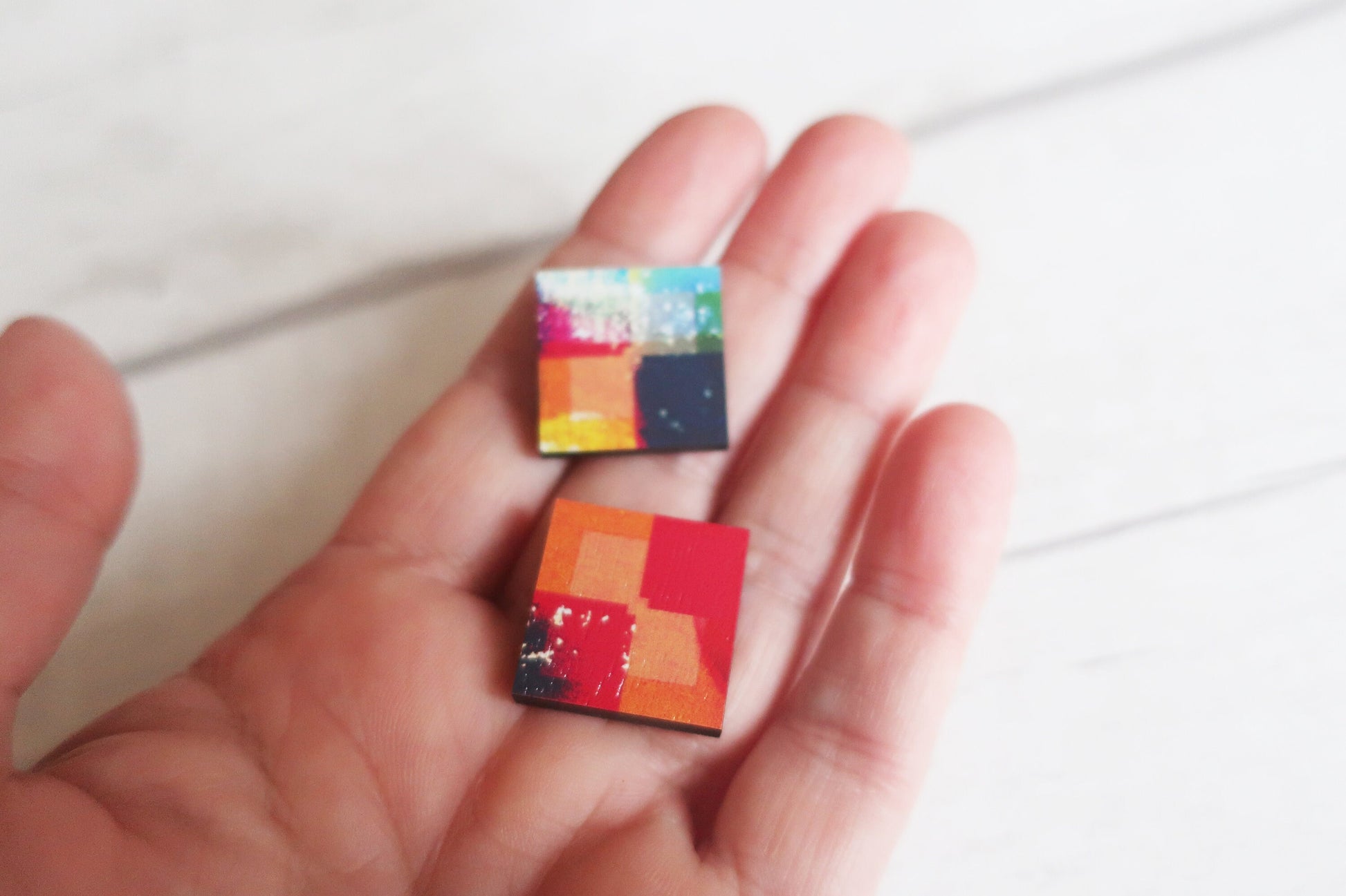Colorful square earrings held in a hand against a white background
